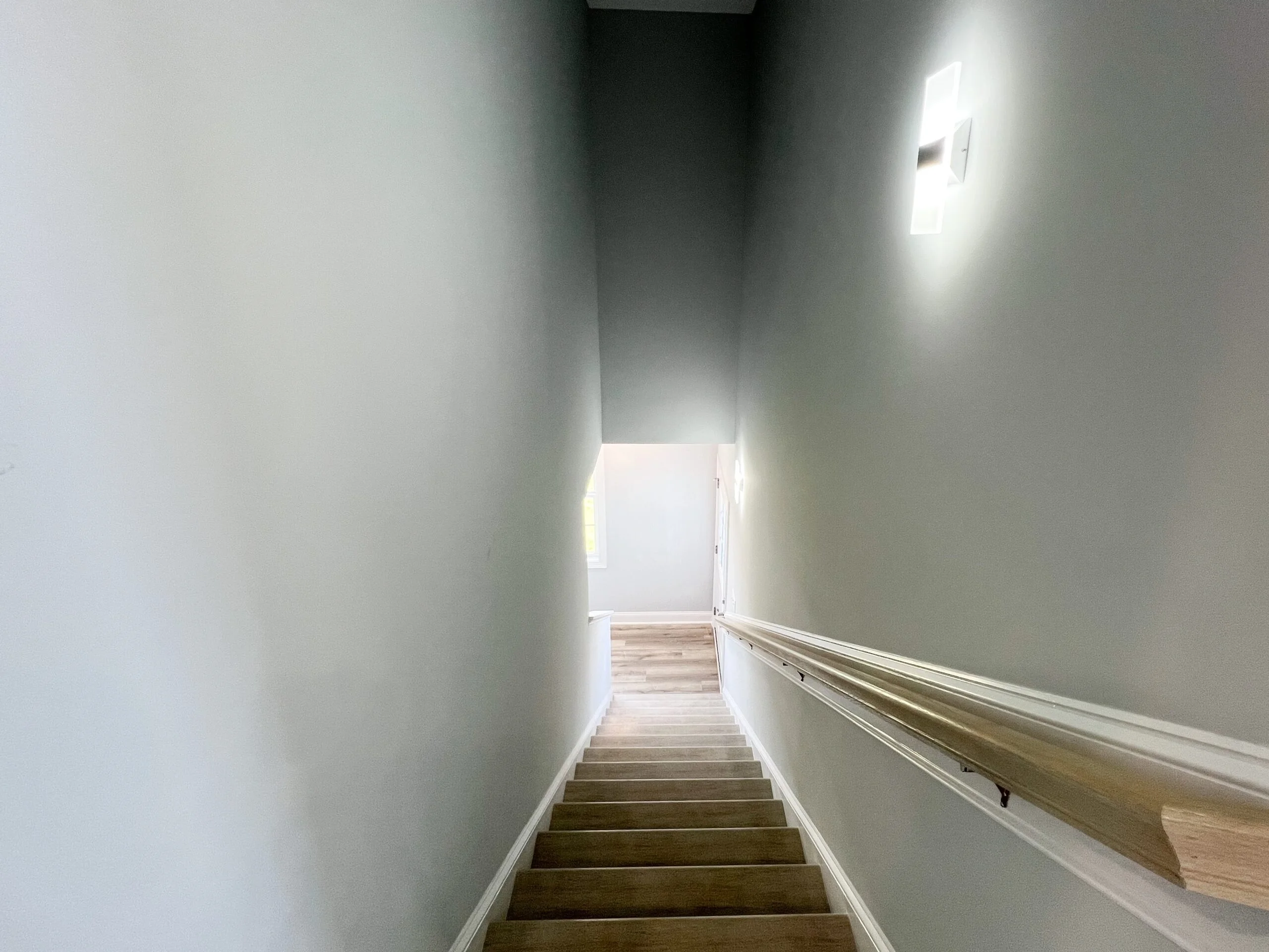 Interior stairwell with gray painted walls, wooden handrail, and finished wood treads