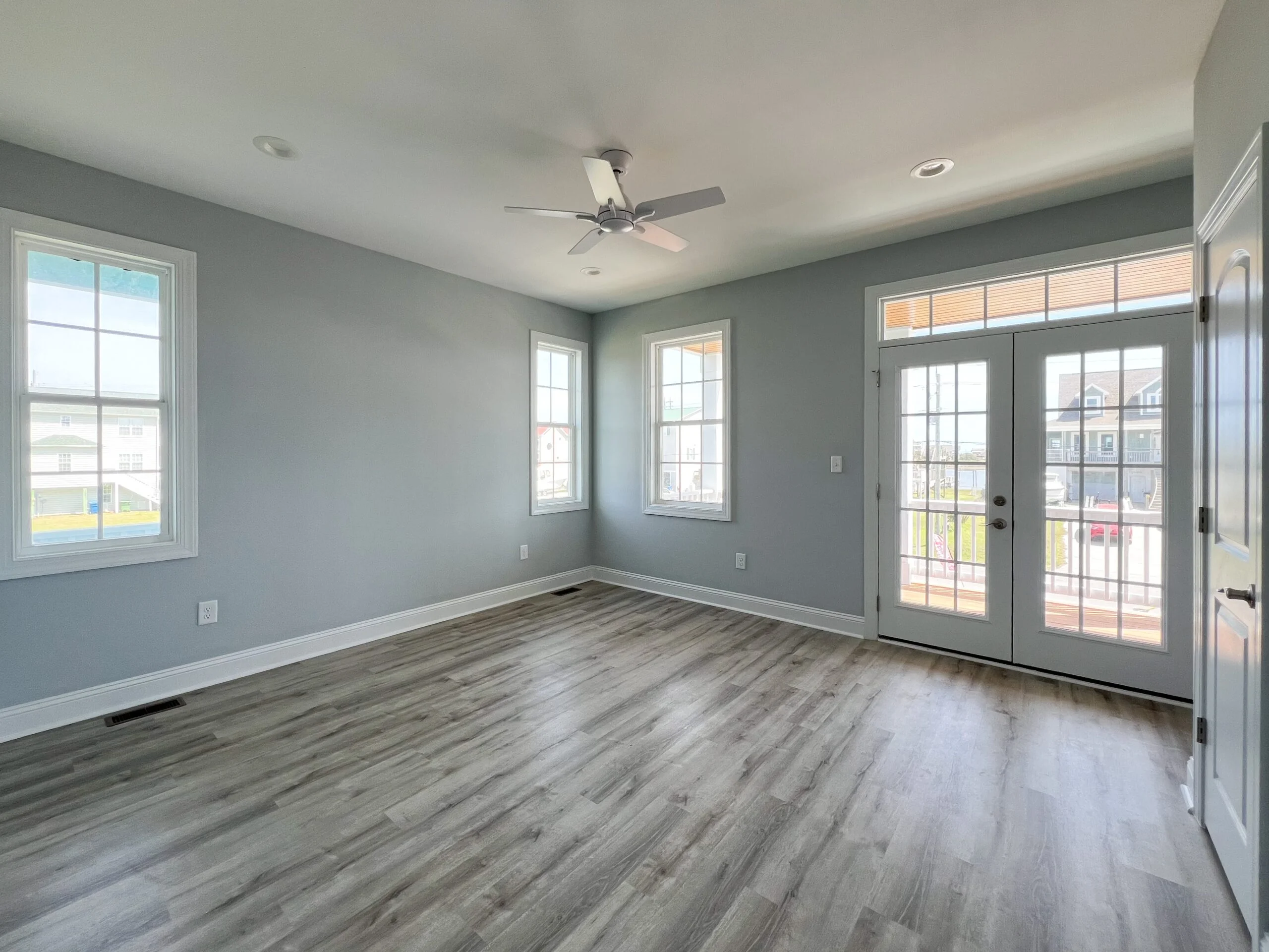 Gray painted room with luxury vinyl plank flooring, white trim, recessed lights, and French doors