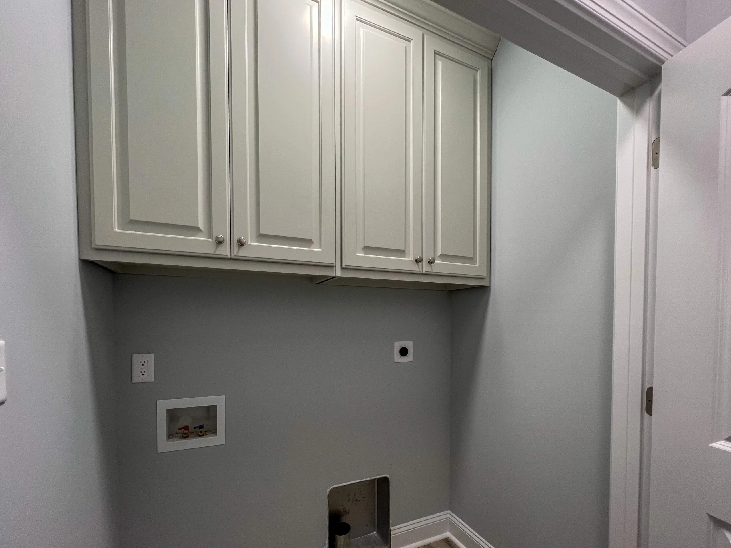 White painted cabinets with recessed panels installed above gray drywall in laundry room
