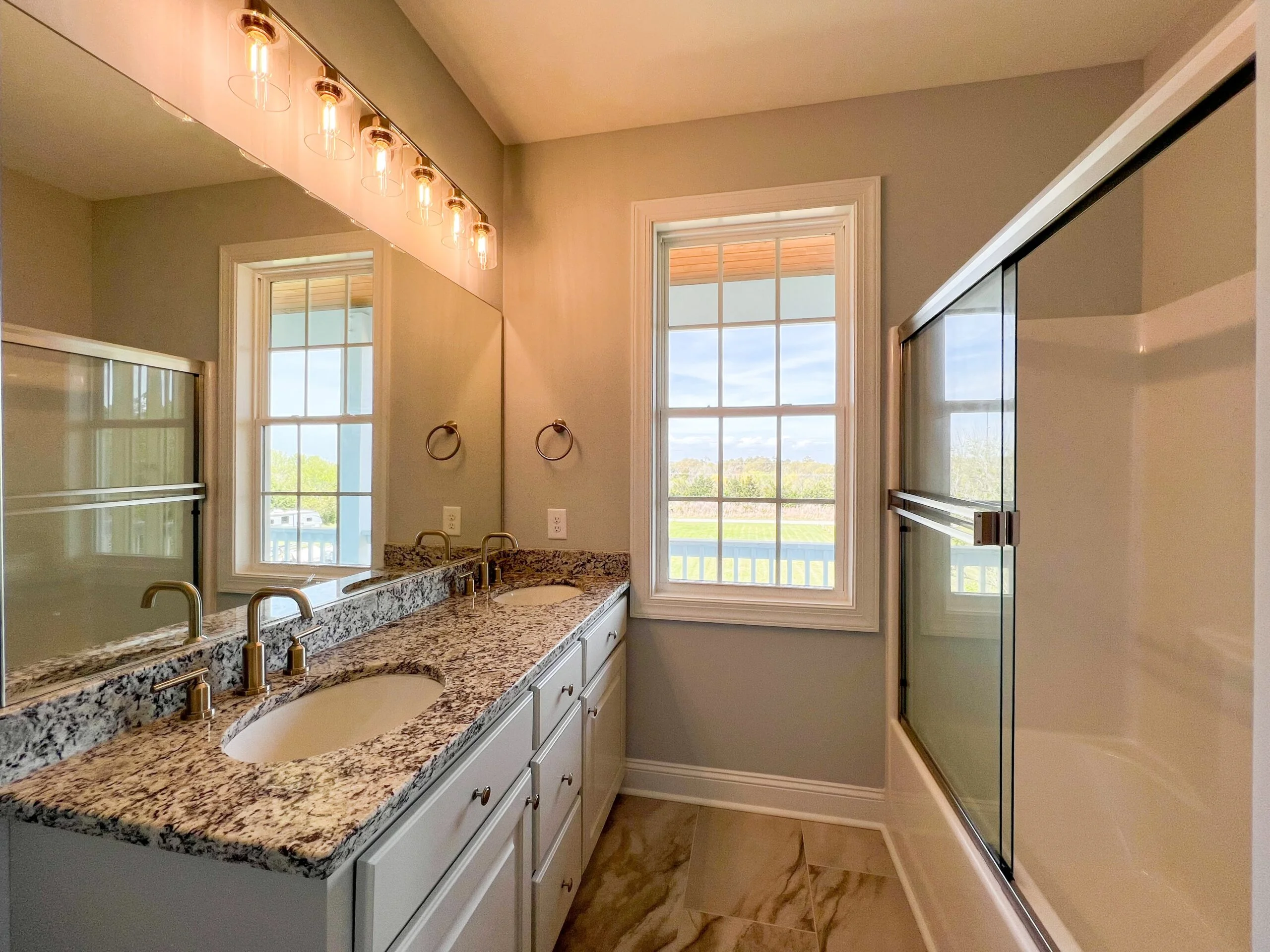 Master bathroom with granite counters, dual sinks, white cabinetry, and frameless glass shower