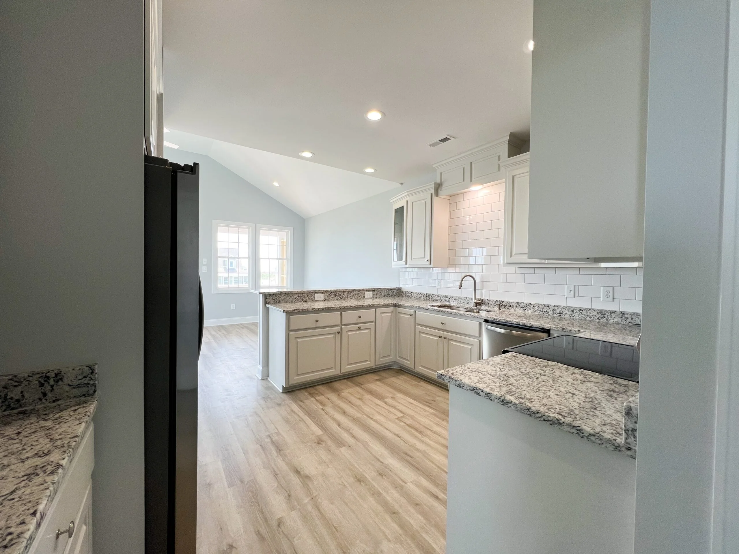 Kitchen with cream cabinets, granite counters, subway tile backsplash, and vinyl plank flooring