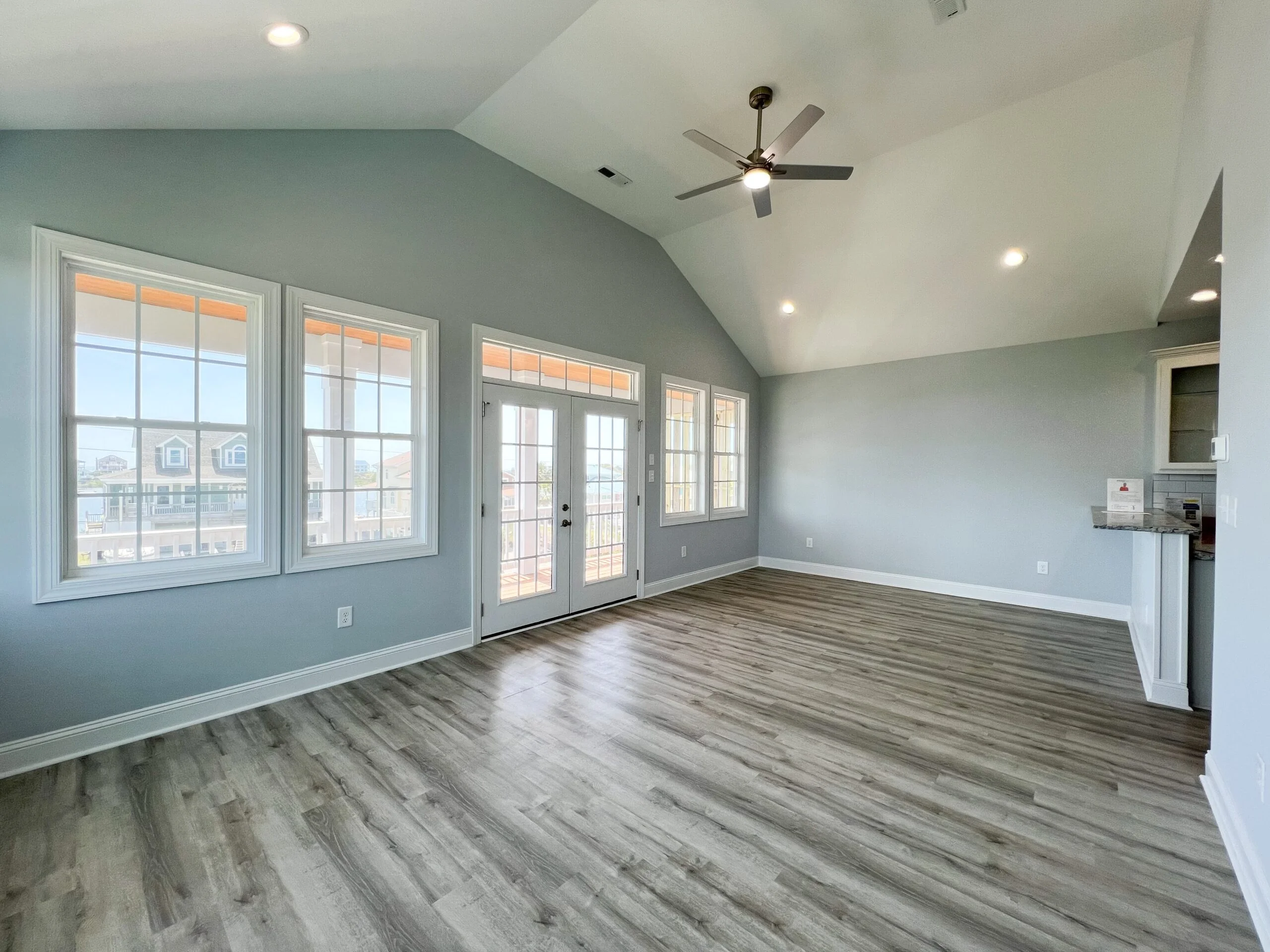 Vaulted ceiling great room with vinyl plank flooring, multi-pane windows, and glass doors