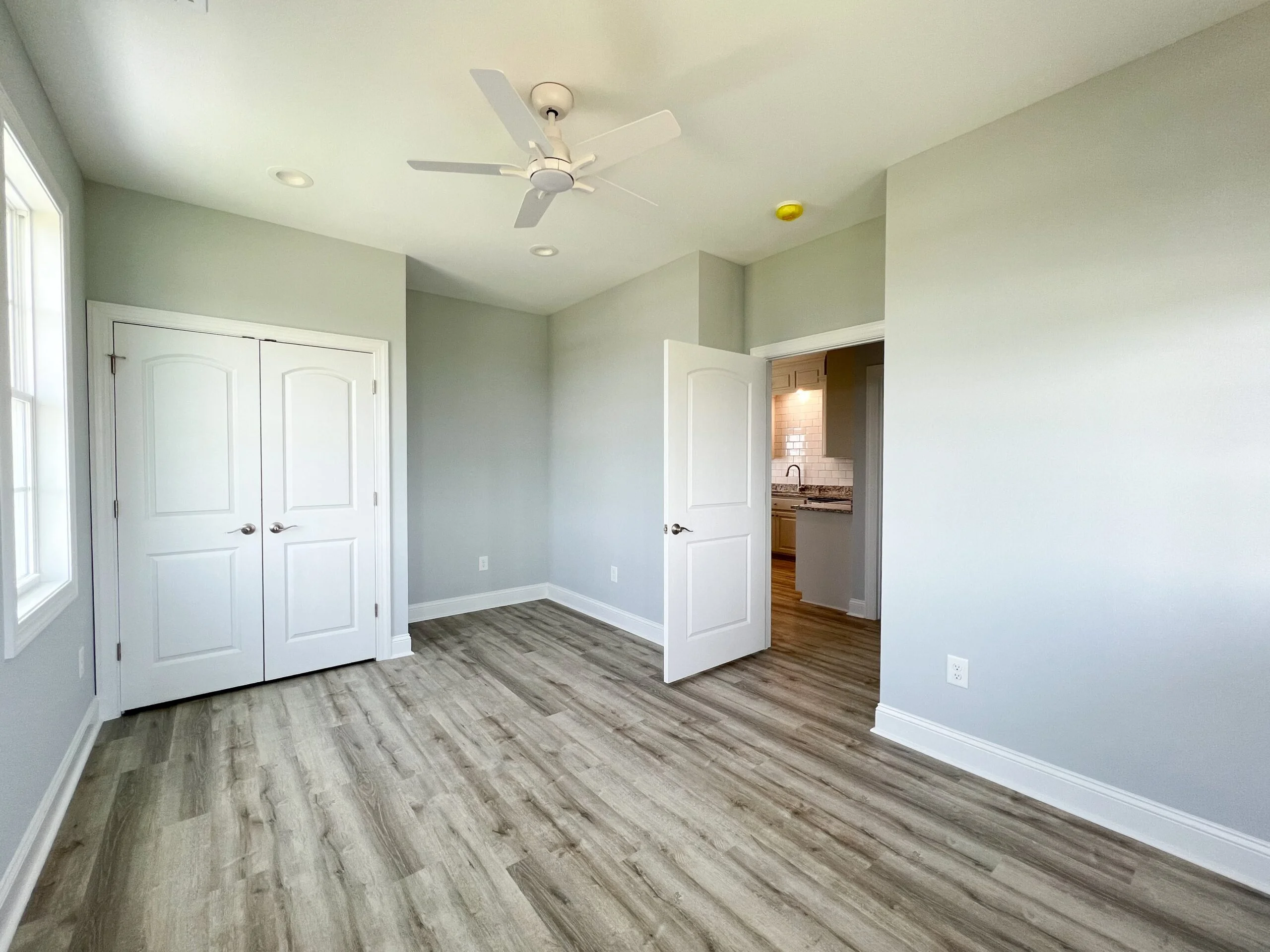 Master bedroom with vinyl plank flooring, sage walls, white doors, and ceiling fan