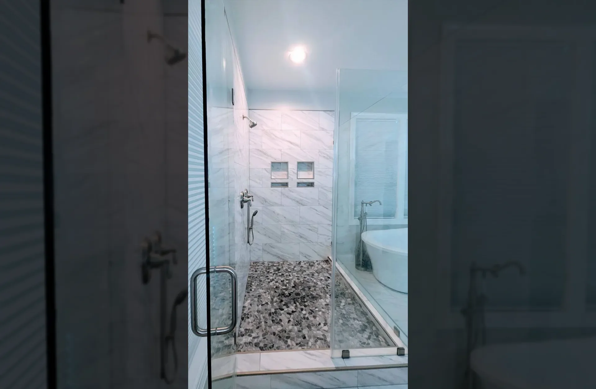 Frameless glass shower with marble tile walls, pebble stone floor, and chrome fixtures