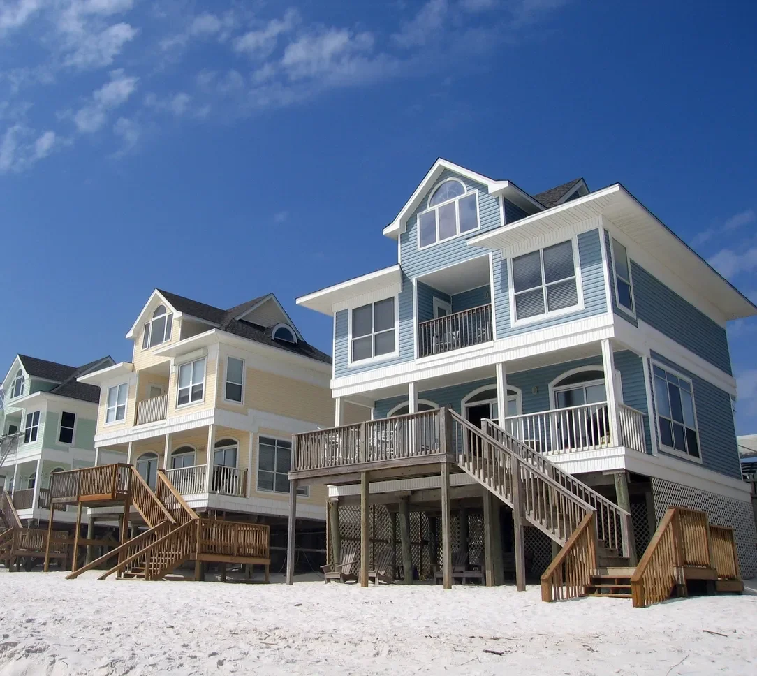 Elevated coastal home with vinyl siding, composite decking, and metal railings on sandy foundation