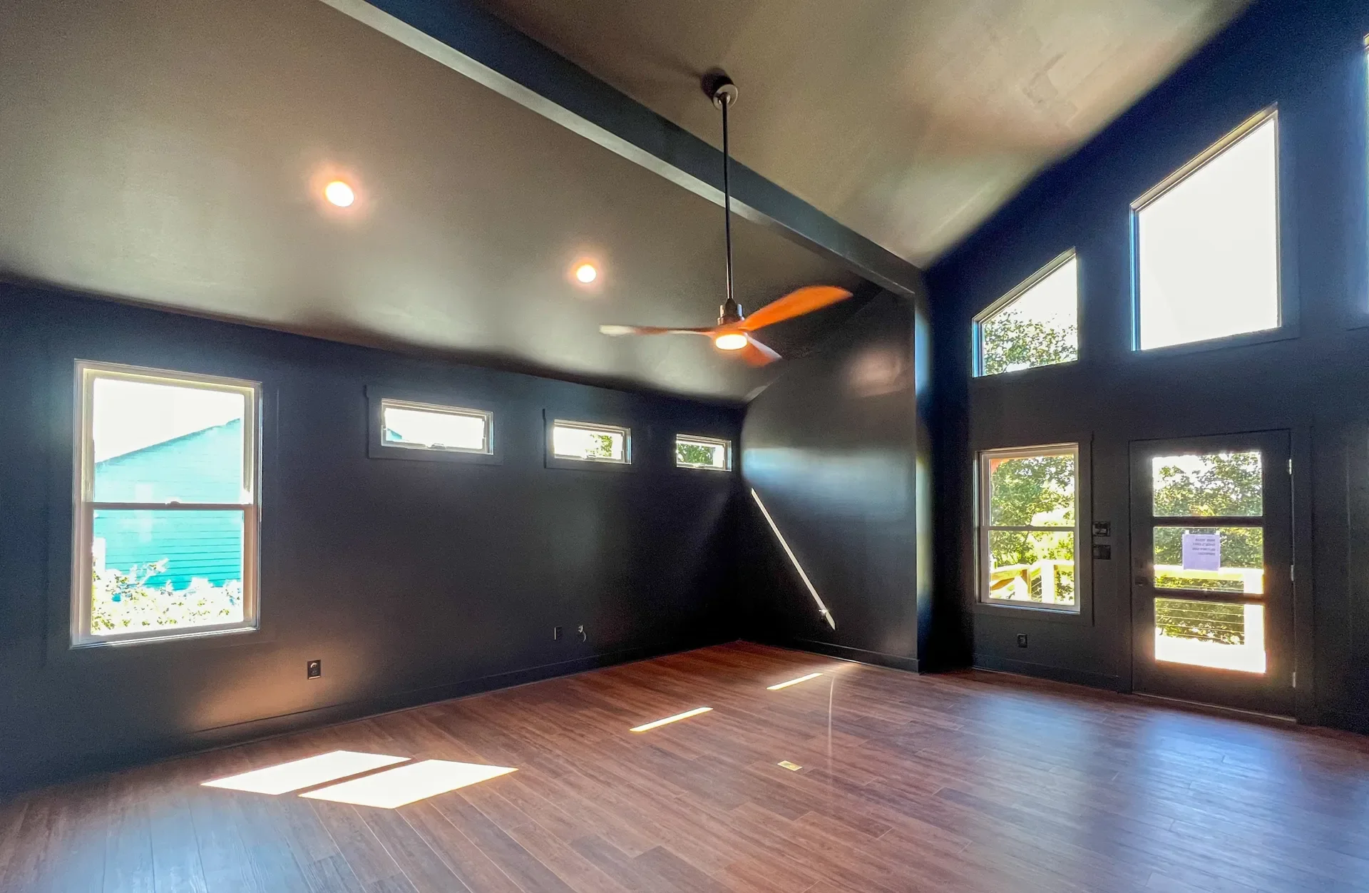 Interior room with navy walls, hardwood floors, recessed lights, ceiling fan, and multiple windows