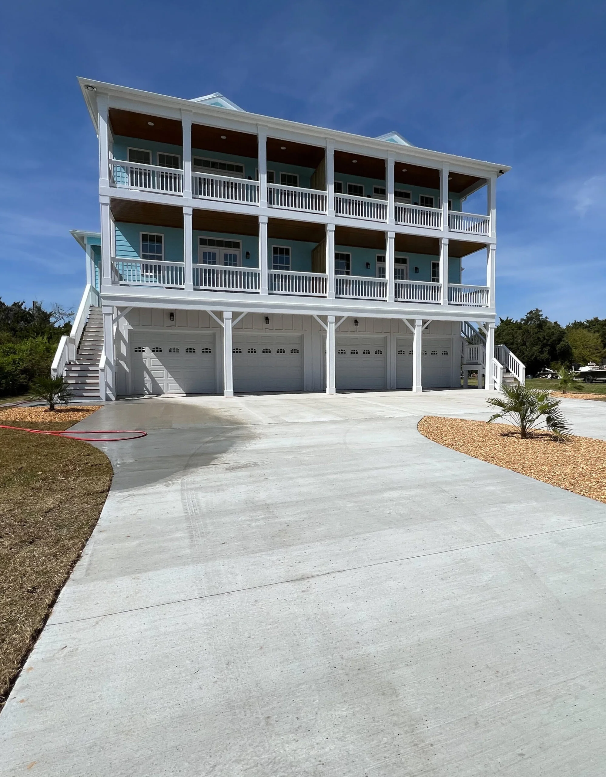 White elevated home with three-car garage, covered decks, and concrete driveway