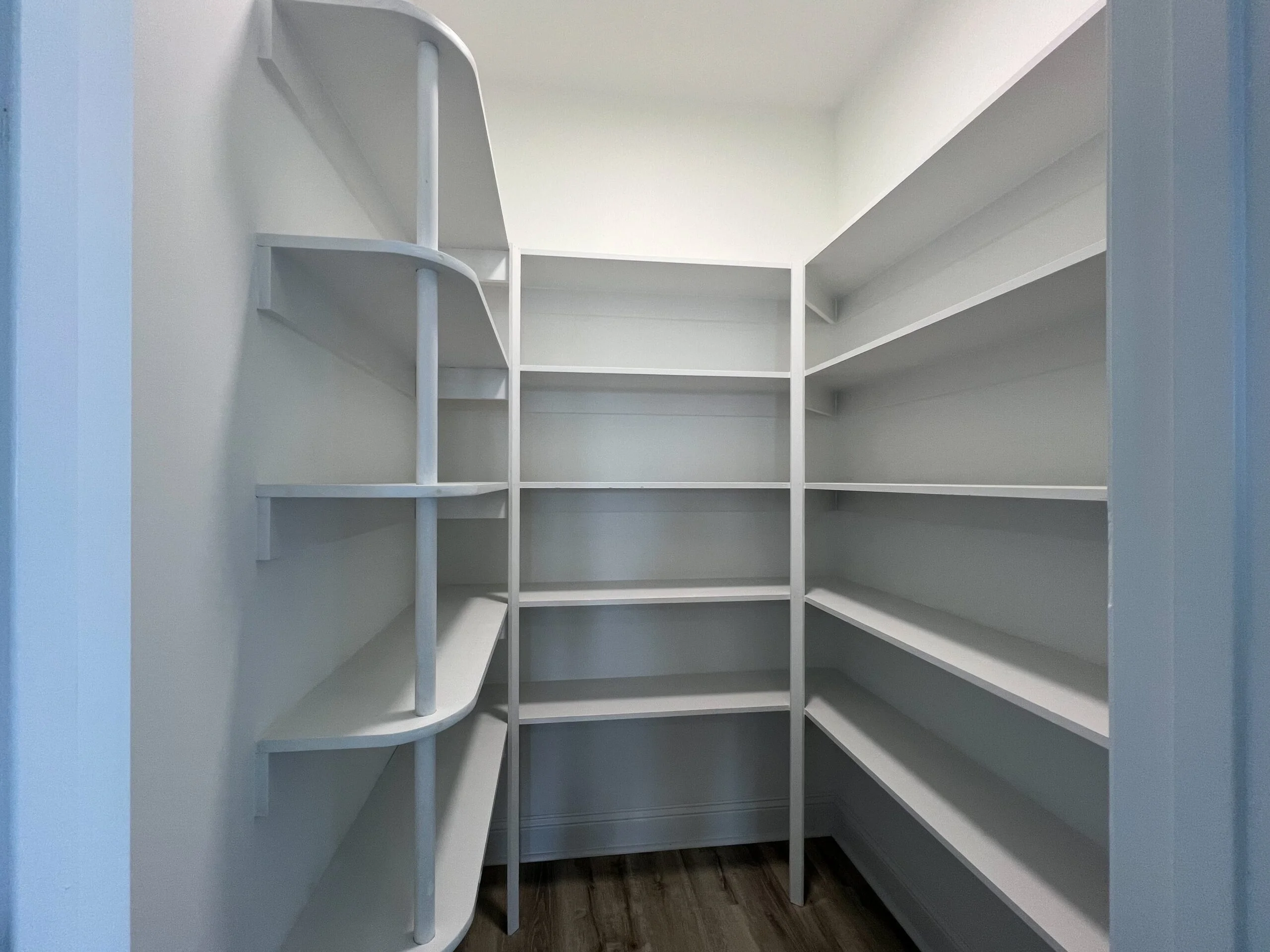White built-in corner shelving with curved design and multiple horizontal shelves in storage space