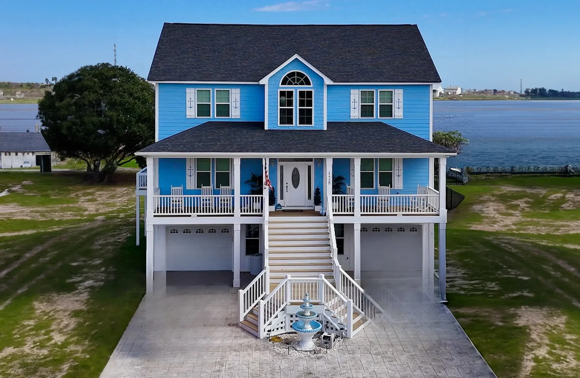 Blue and white elevated waterfront home with covered porches, dual garages, and composite decking