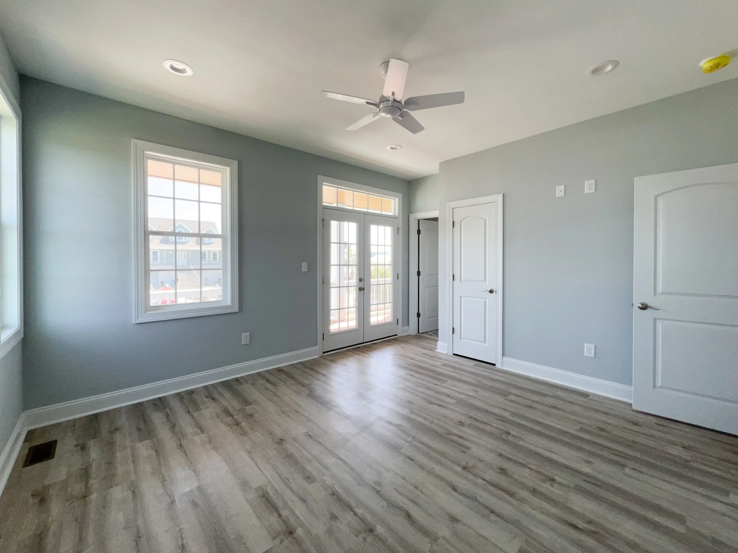 Master suite with vinyl plank flooring, gray walls, white trim, and French doors