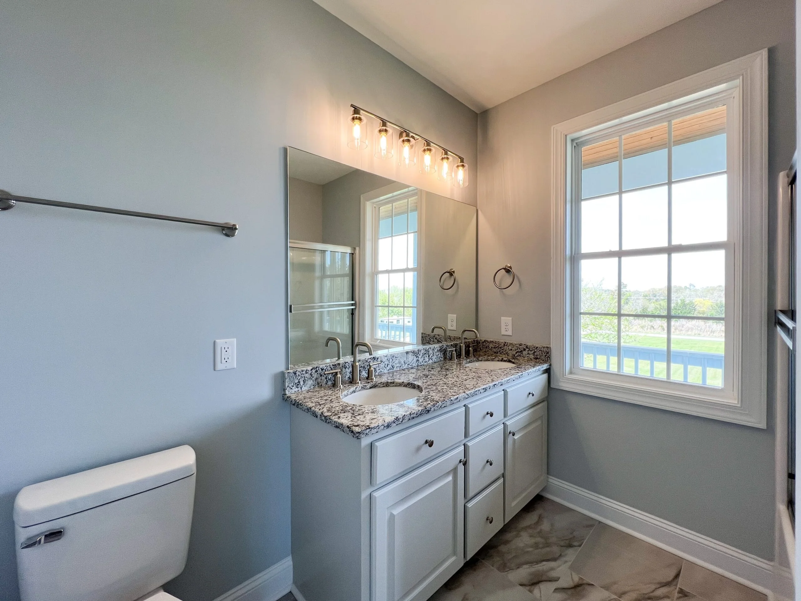 Dual-sink bathroom vanity with granite countertop, white cabinetry, and frameless glass shower