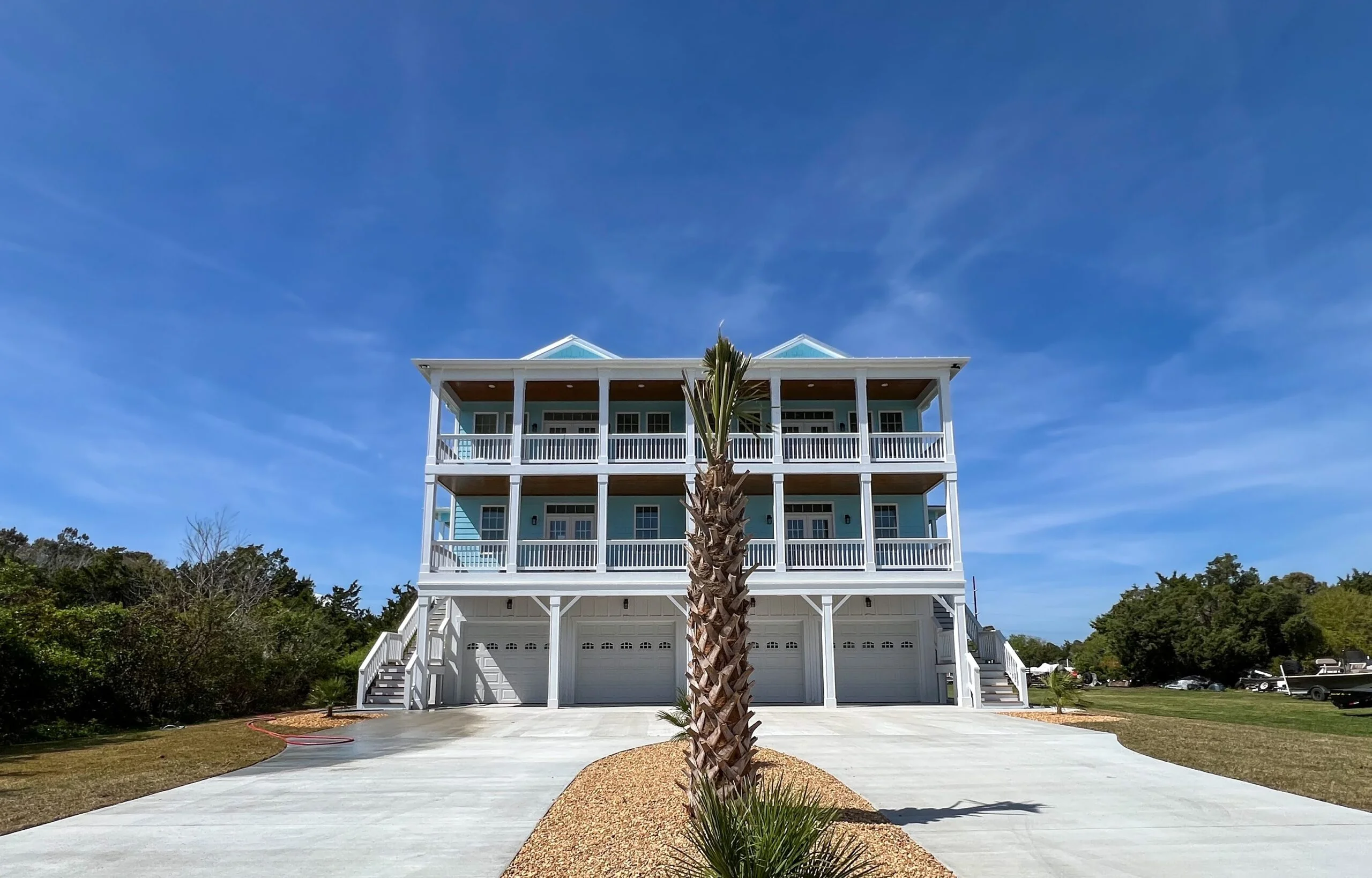 Three-story white coastal home with covered porches, white railings, and four-bay garage