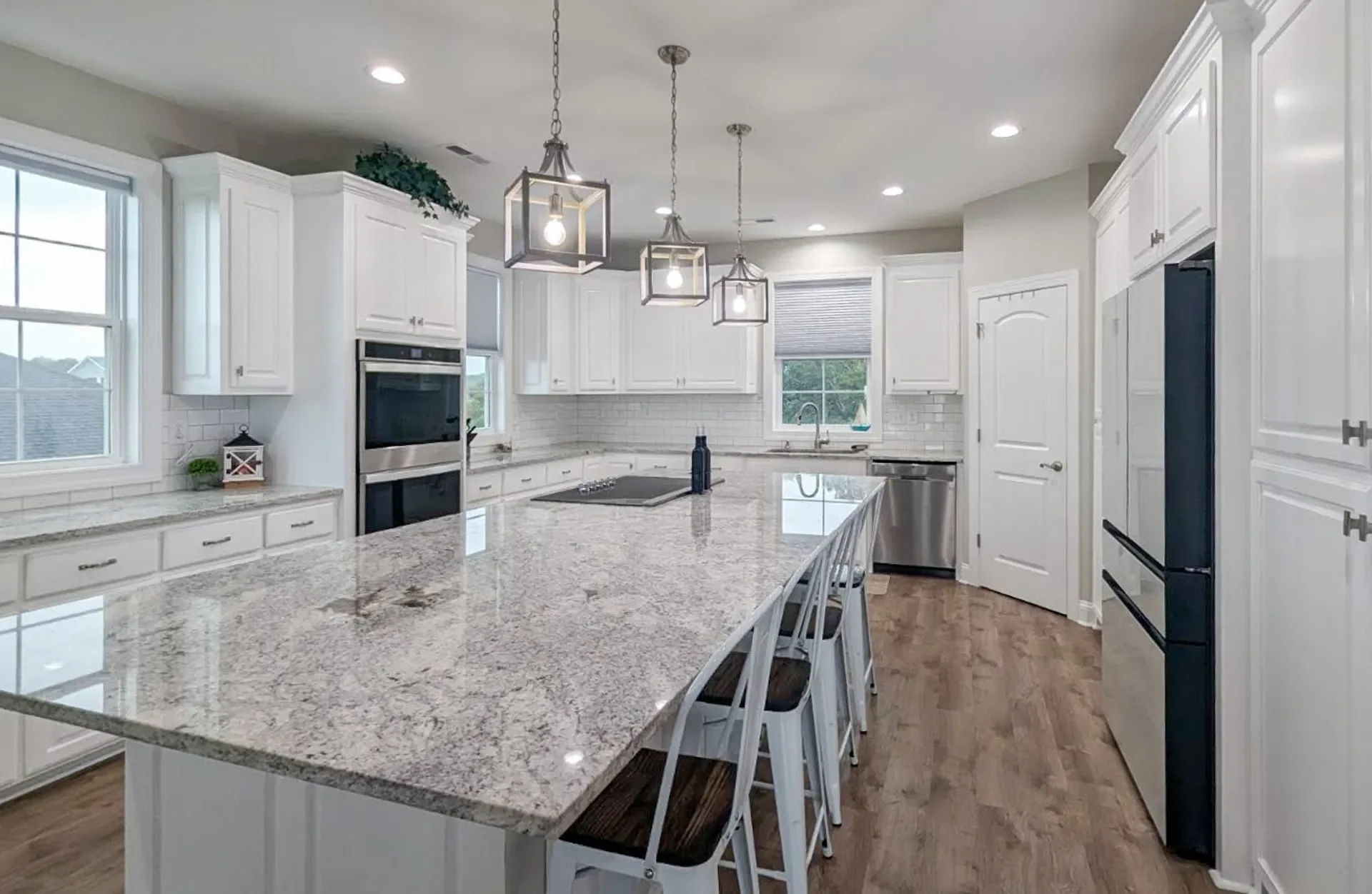 White kitchen with granite island, stainless steel appliances, pendant lights, and subway tile backsplash