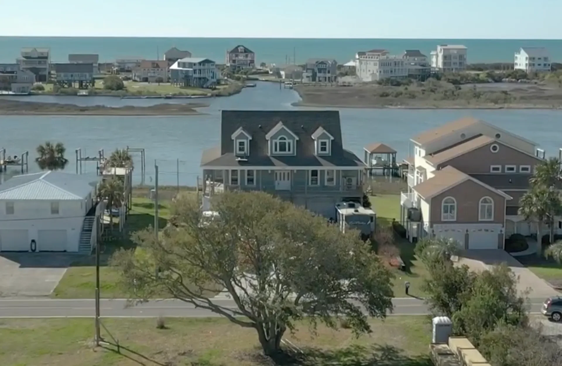Dark-roofed colonial home with three dormers, elevated foundation, and waterfront setting