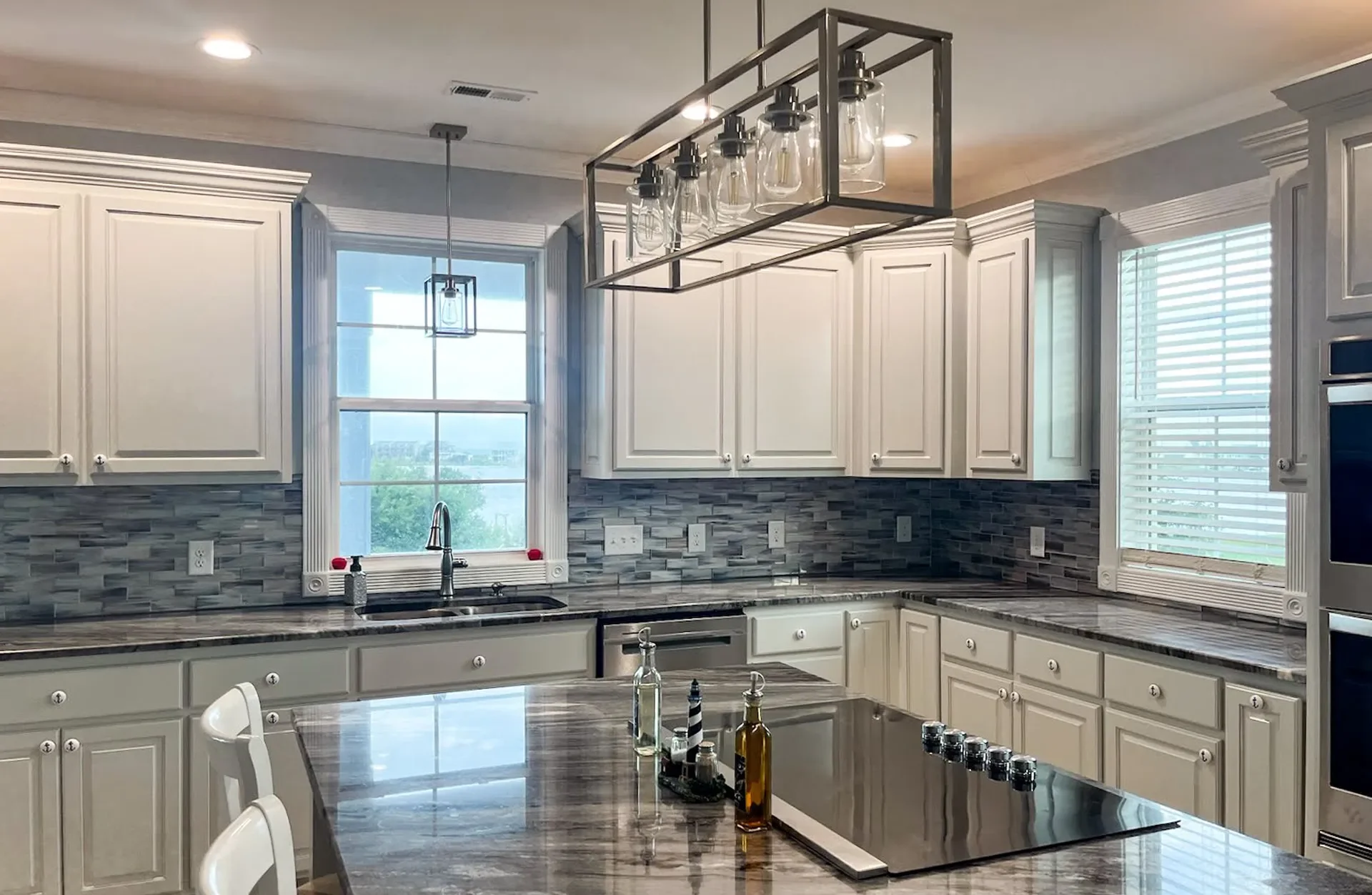 Kitchen with cream cabinets, gray tile backsplash, dark granite counters, and linear pendant lighting
