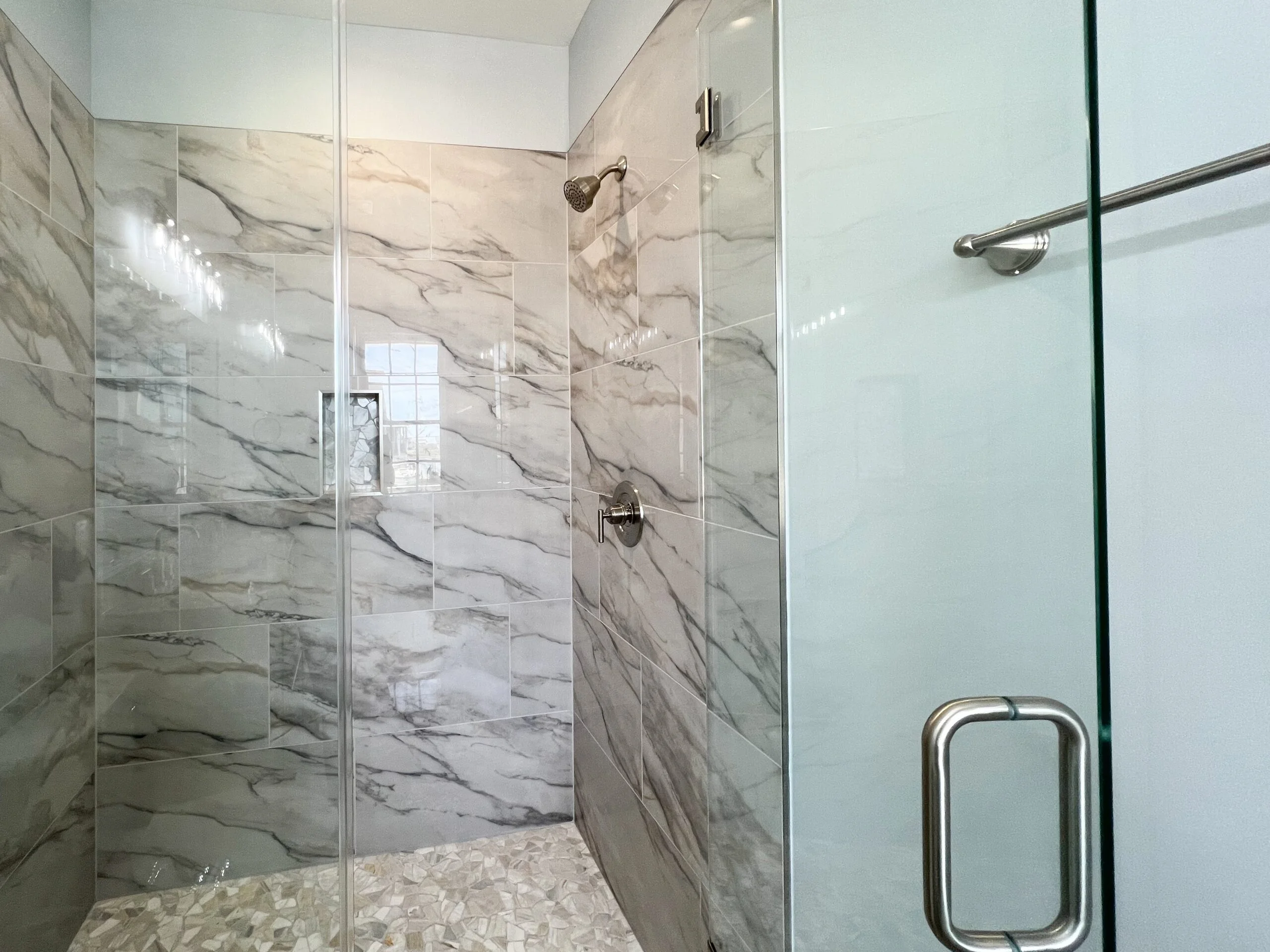 Frameless glass shower with marble veining tile walls and floor, brushed nickel fixtures