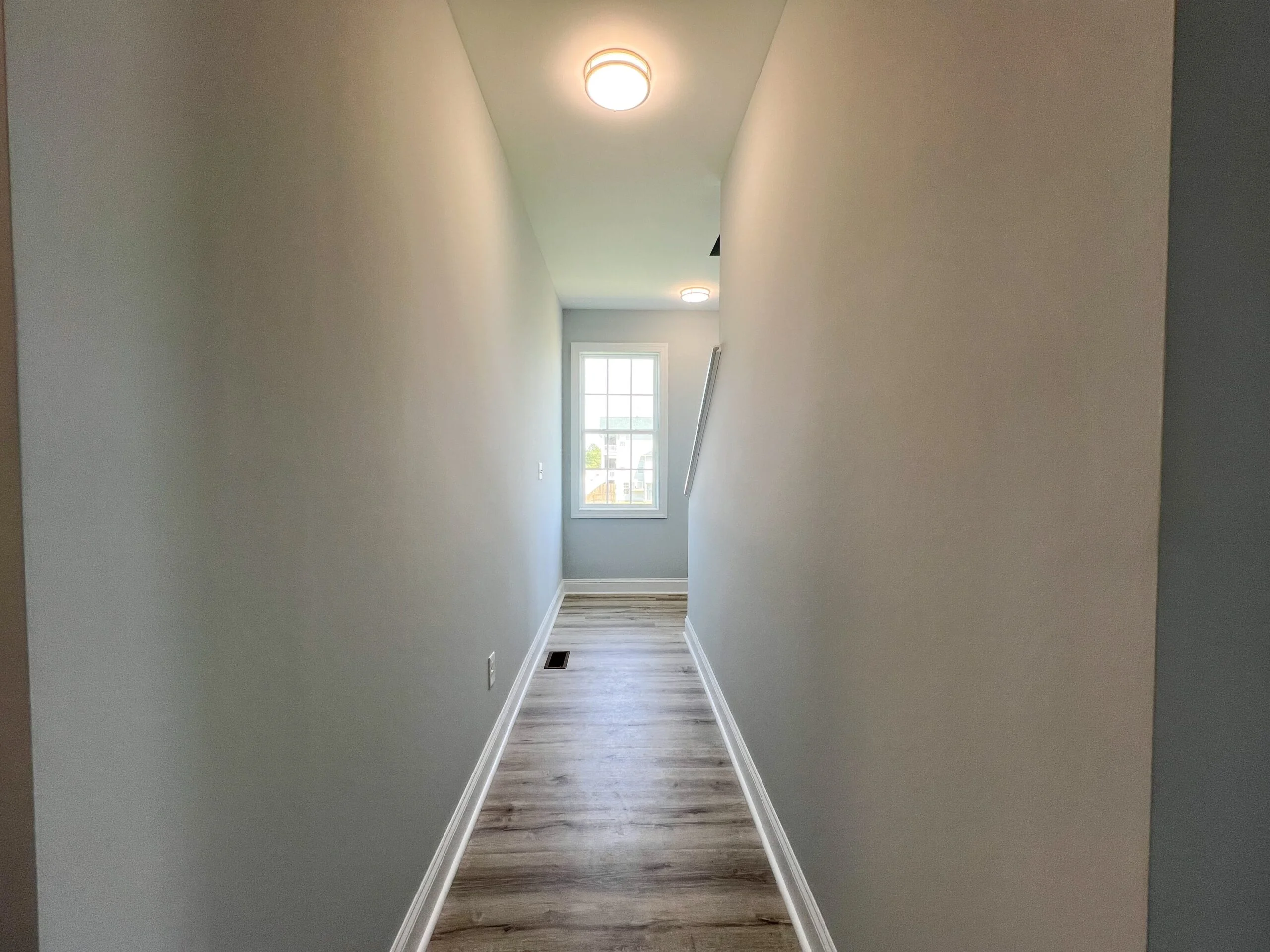 Finished hallway with white drywall, recessed lighting, and laminate flooring with trim