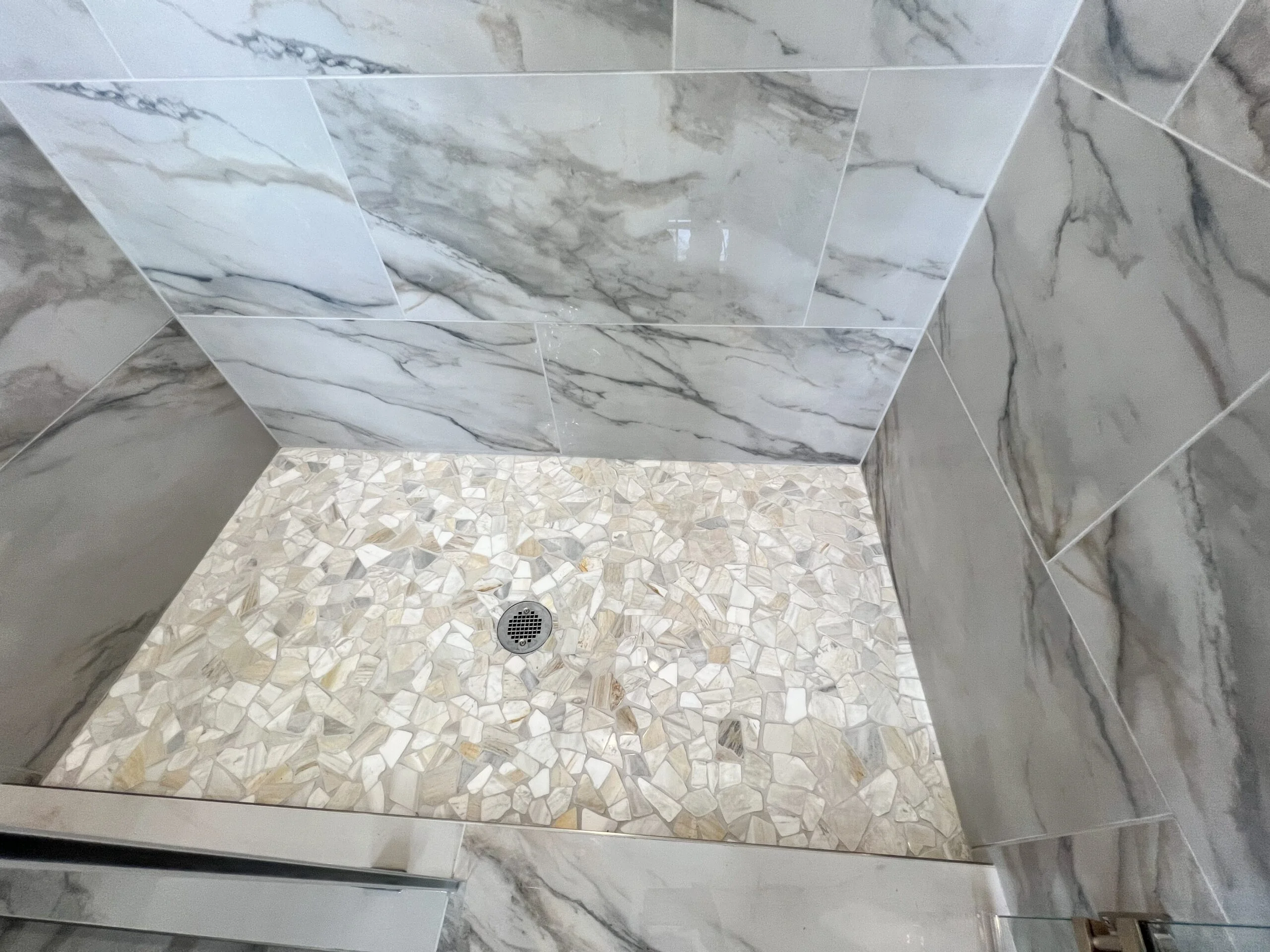 Marble subway tile shower walls with cream mosaic tile floor and chrome drain
