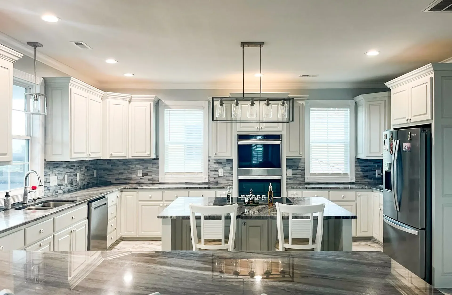 White kitchen cabinets, blue tile backsplash, gray island with quartz countertops and pendant lighting