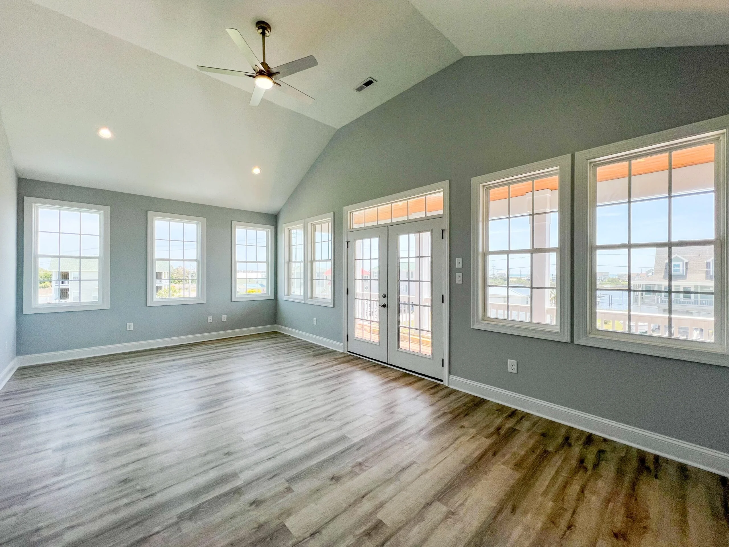 Vaulted ceiling room with vinyl plank flooring, recessed lights, ceiling fan, and multiple windows