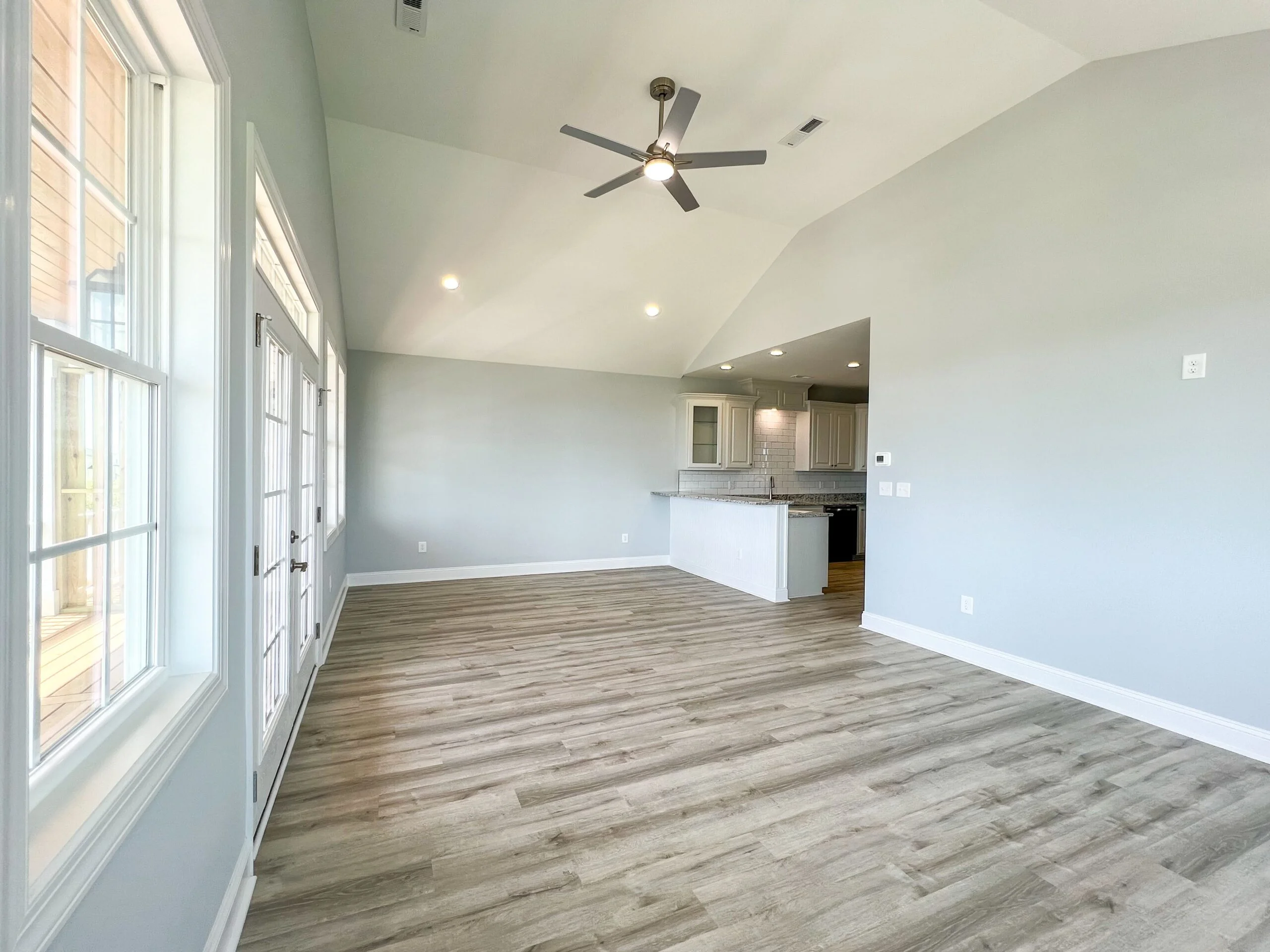 Open concept room with wood-look vinyl flooring, vaulted ceiling, recessed lights, ceiling fan, and adjacent kitchen with white cabinets