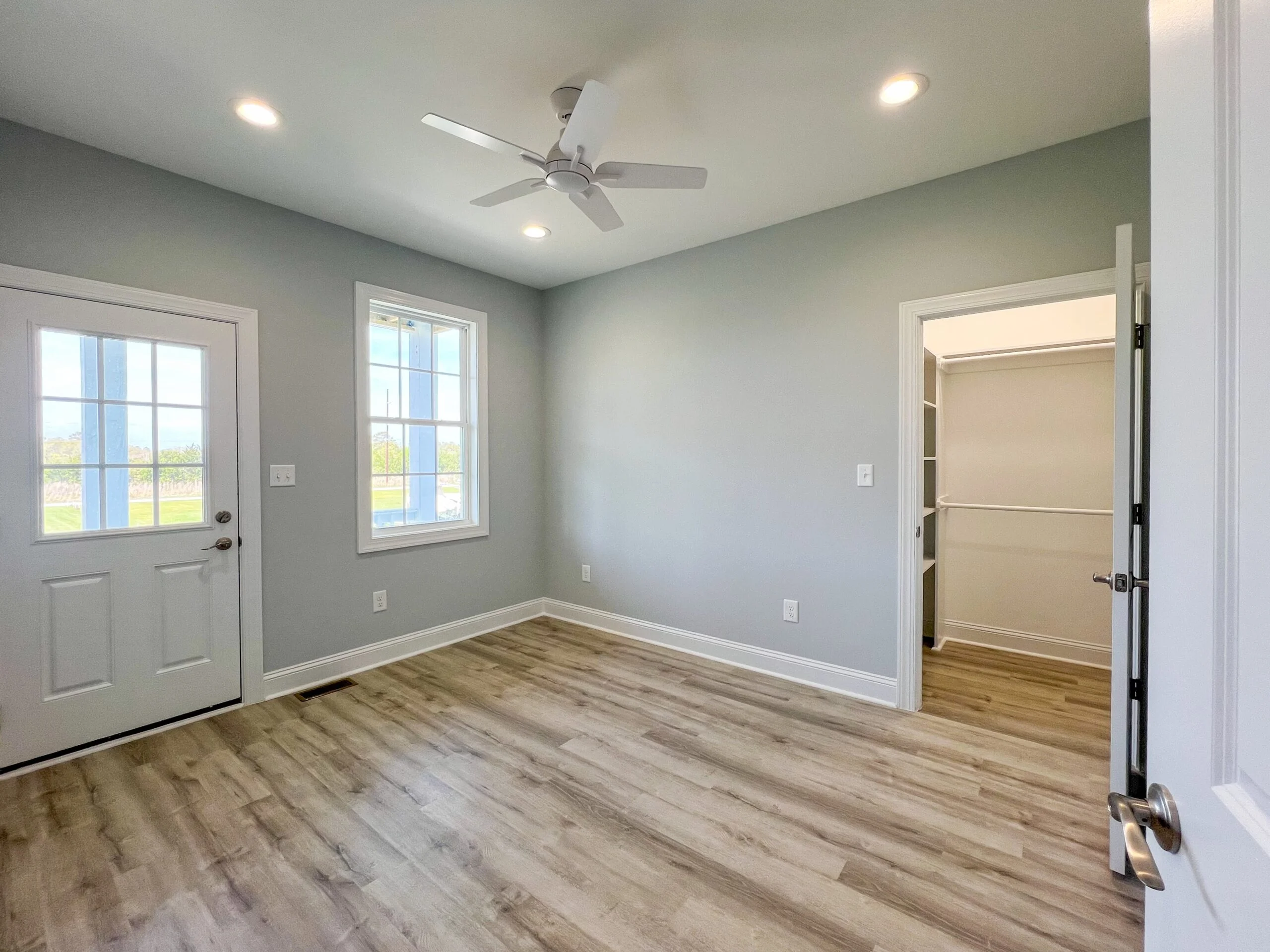 Spacious bedroom with vinyl plank flooring, gray walls, white trim, recessed lights, and ceiling fan