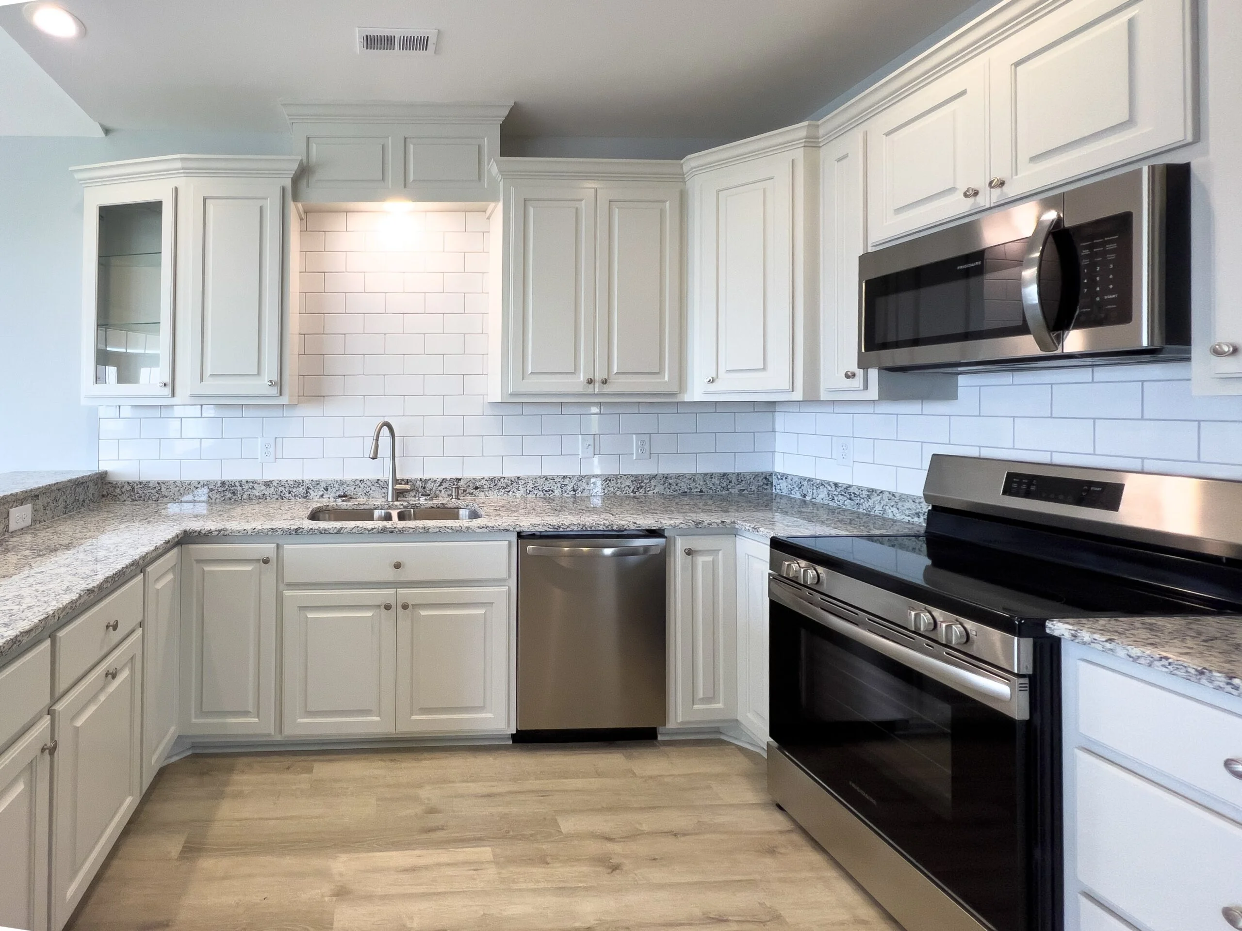 White kitchen cabinets, granite countertops, subway tile backsplash, stainless steel appliances