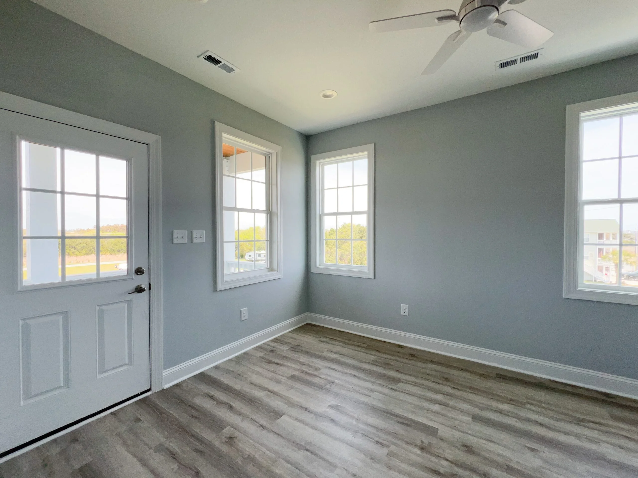 Interior room with gray walls, white trim, laminate flooring, multiple windows and glass door