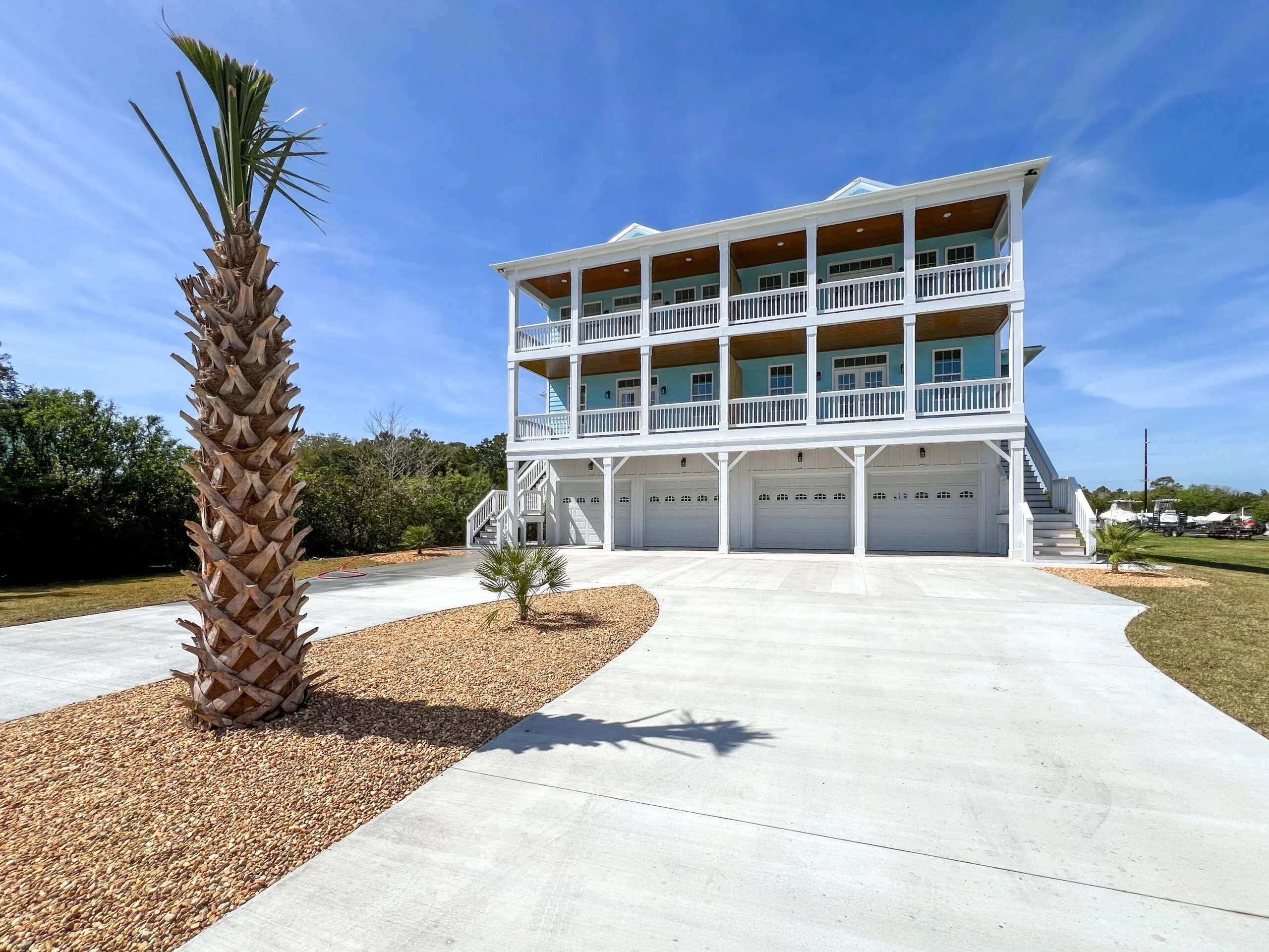 Three-story elevated home with white trim, blue siding, three-car garage, and concrete driveway