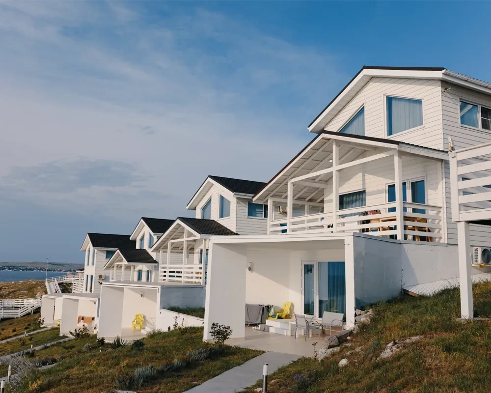 White fiber cement siding beach homes with black roofs, white deck railings, and concrete patios on coastal lot