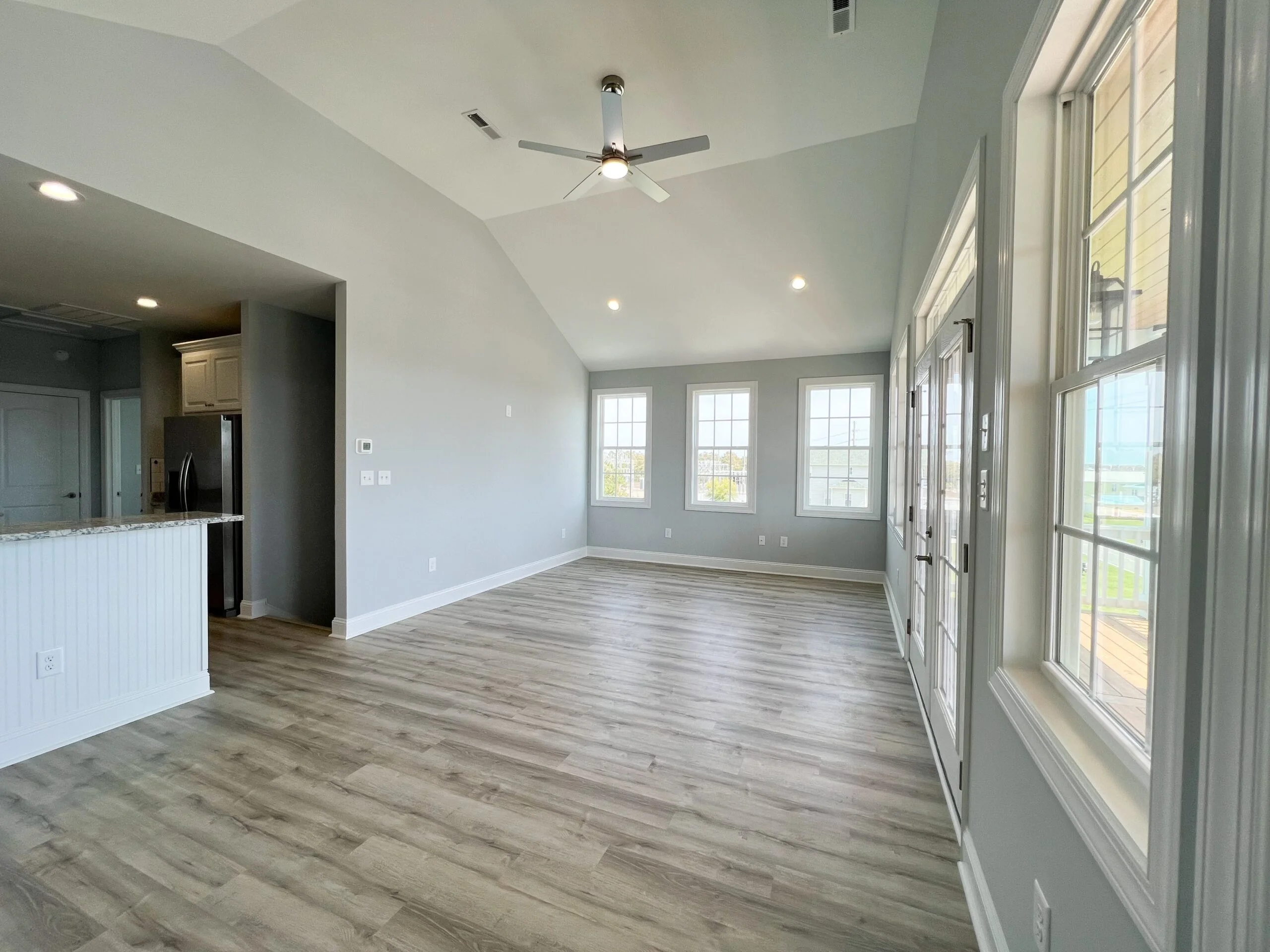 Open living room with vaulted ceiling, vinyl plank flooring, recessed lights, and multi-pane windows