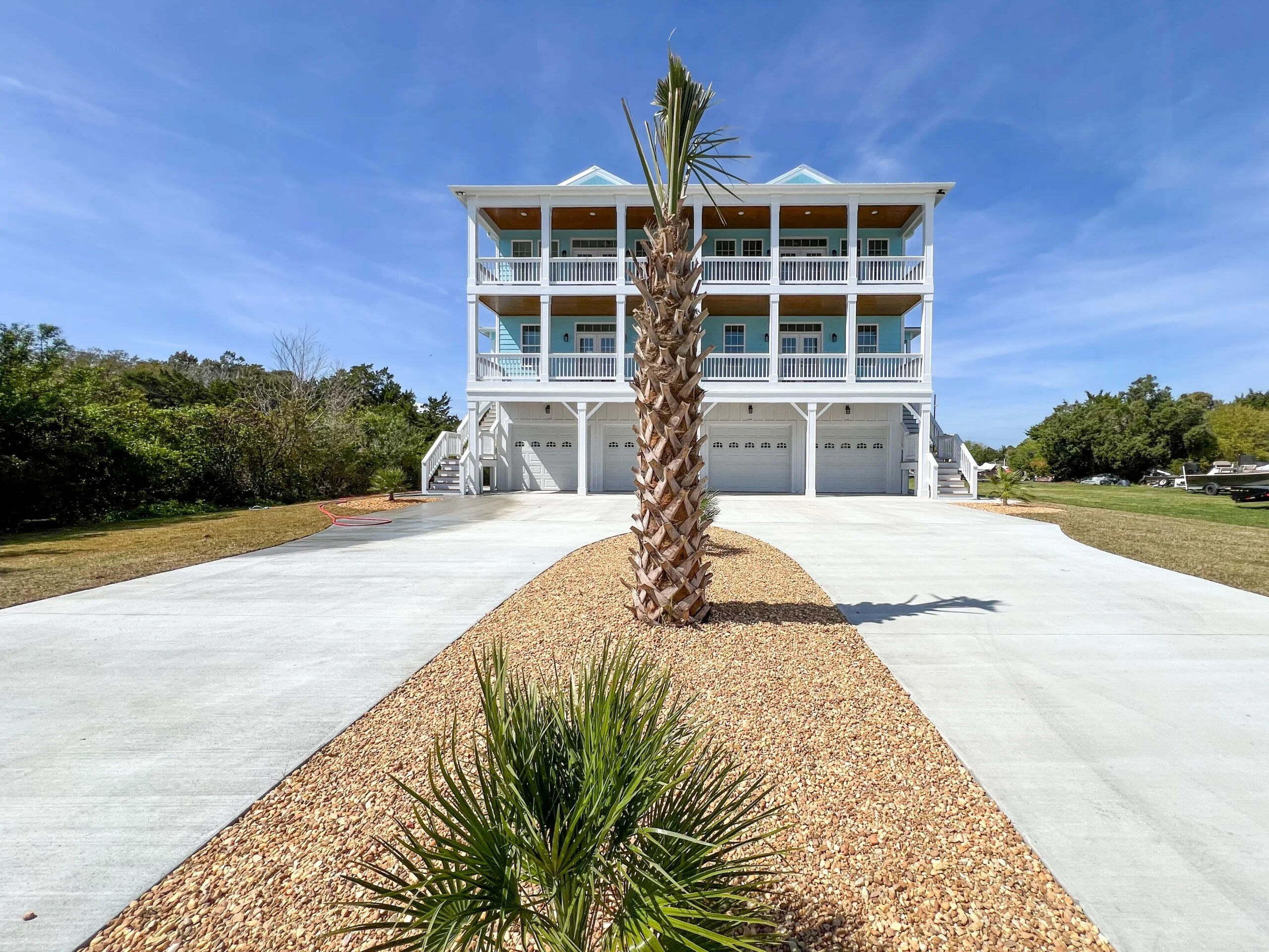 Three-story white elevated residential building with covered balconies, garage bays, and concrete driveway