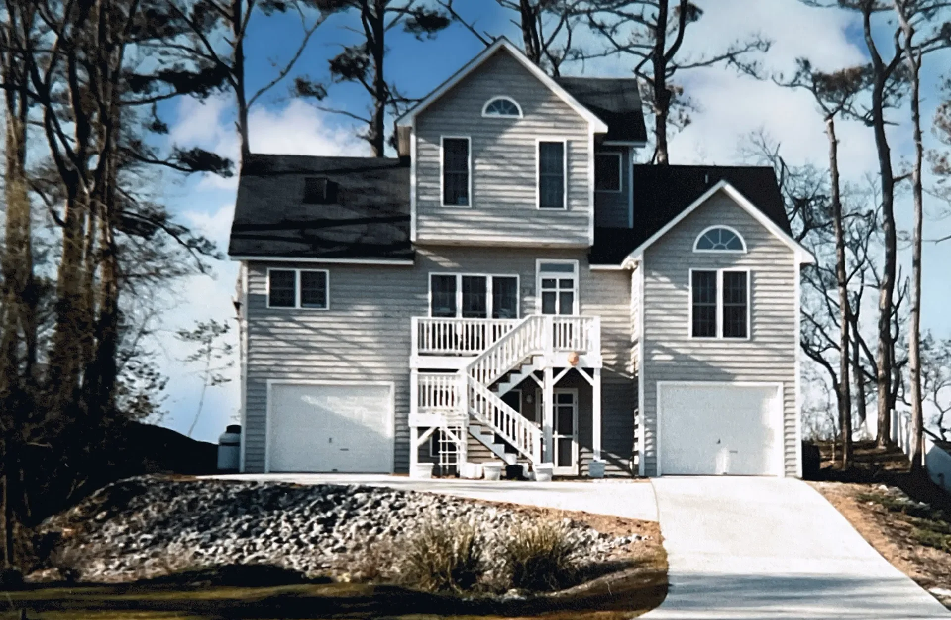 Two-story colonial home with vinyl siding, elevated deck, two-car garage, and gabled rooflines