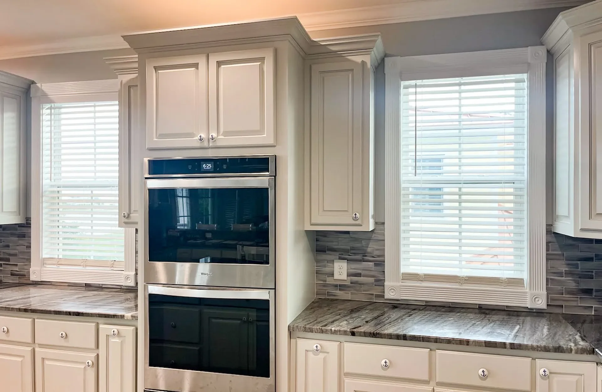Kitchen with cream cabinetry, double wall ovens, granite counters, and tile backsplash
