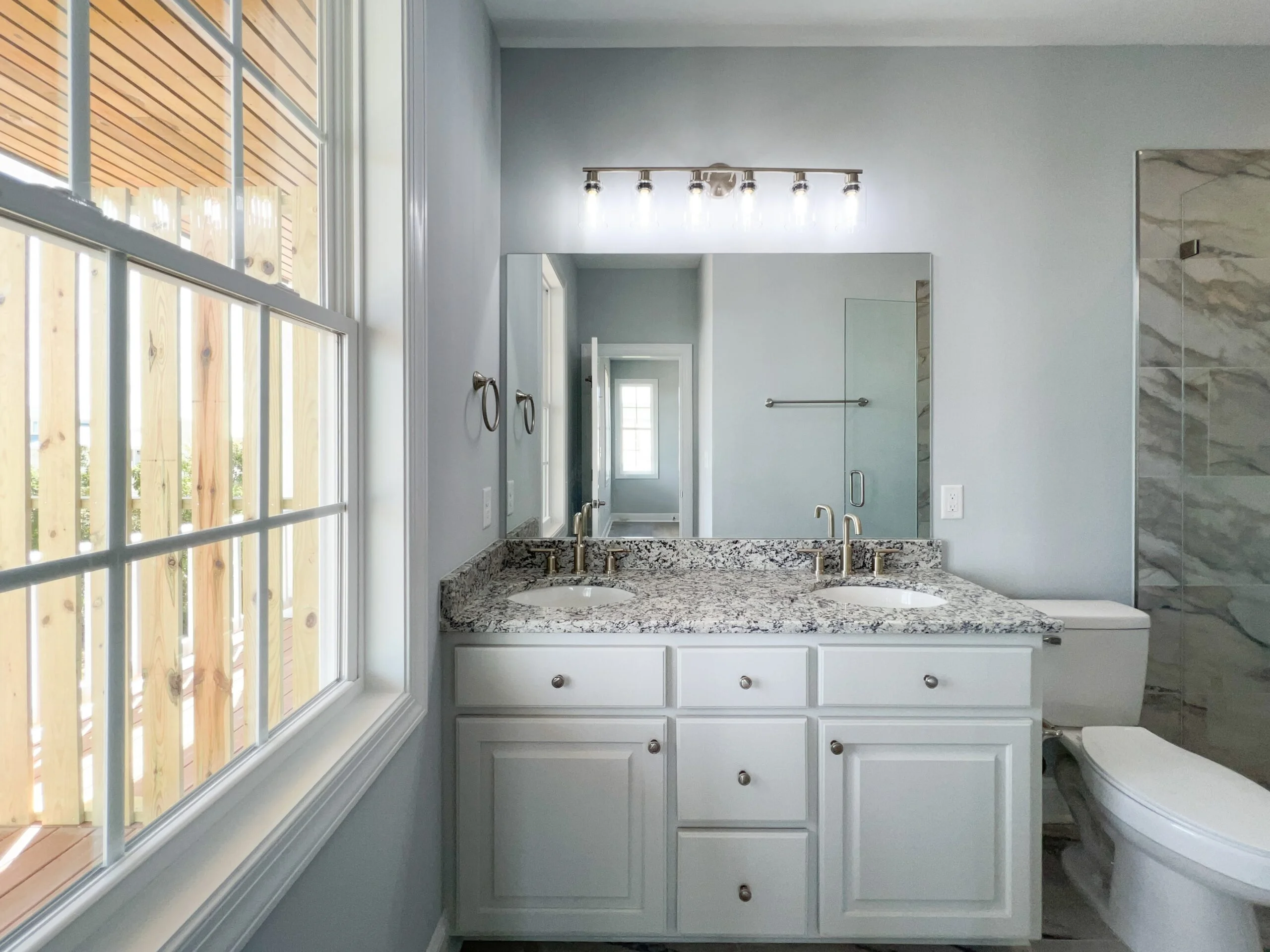 Master bathroom with white dual-sink vanity, granite countertop, frameless glass shower, and chrome fixtures