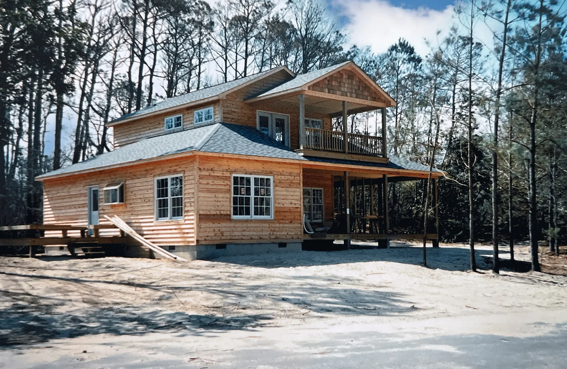 Two-story wood-sided home with gray shingle roof, covered porches, and raised foundation