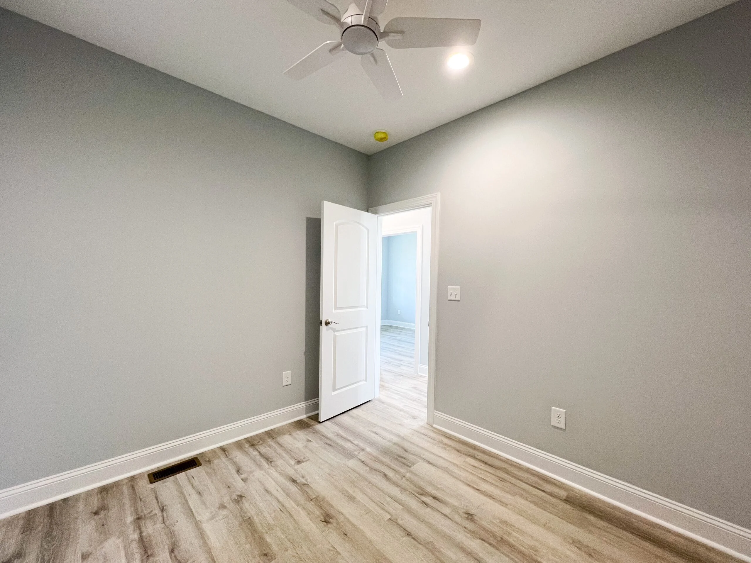 Finished bedroom with gray walls, white doors, vinyl plank flooring, and ceiling fan