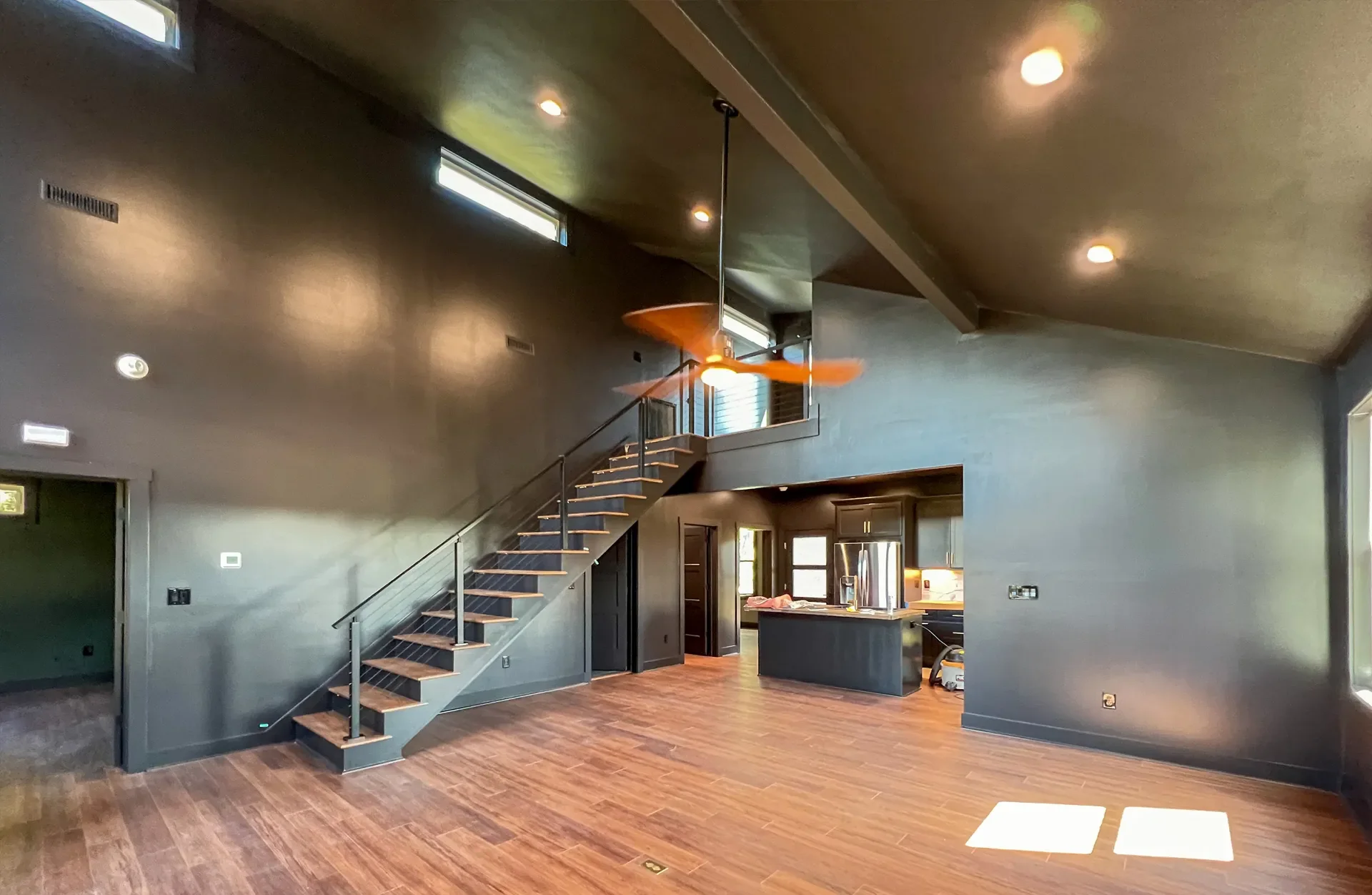Open-concept interior with custom wood and steel staircase, recessed lighting, hardwood flooring, and modern kitchen
