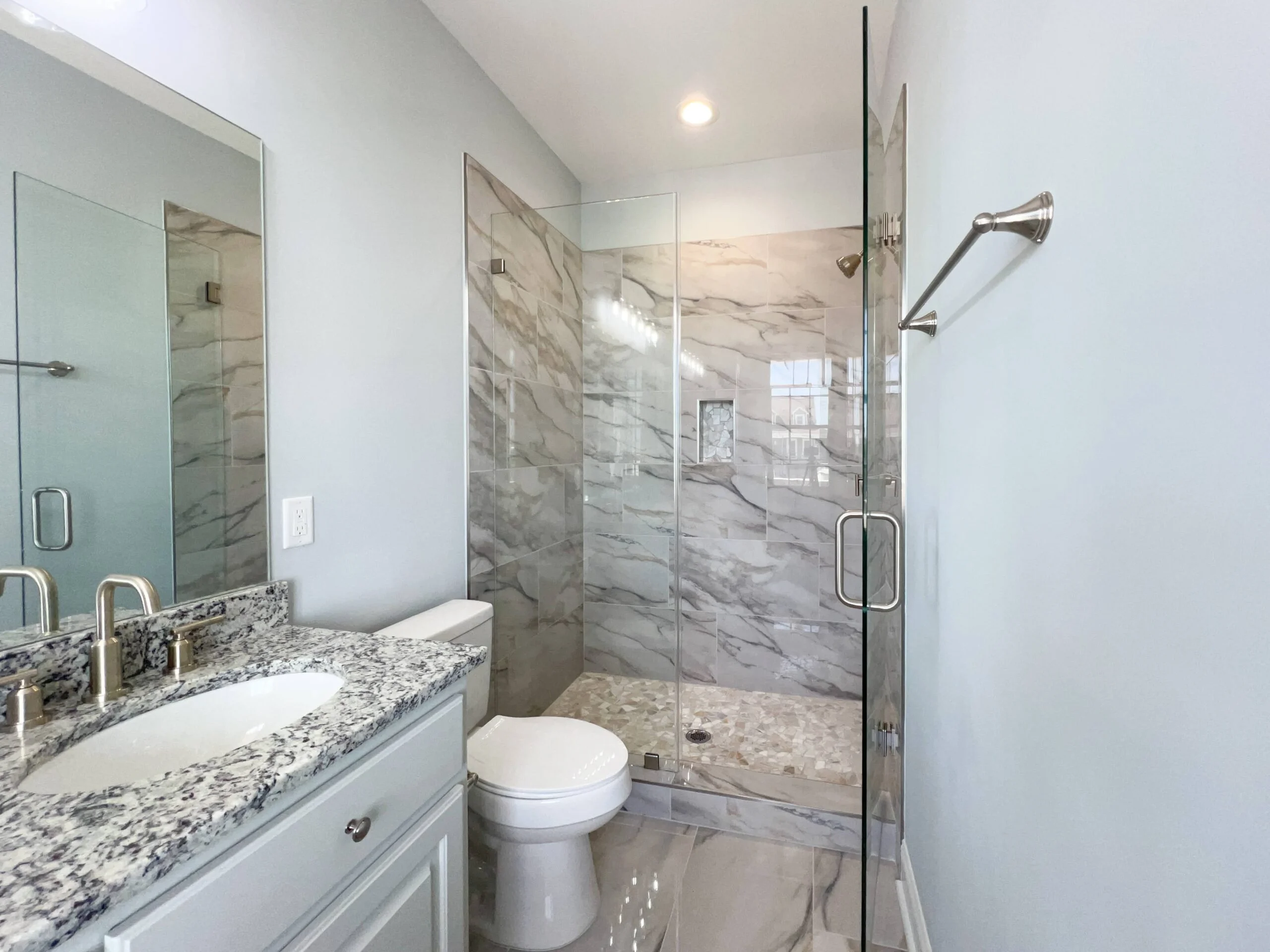 Master bathroom with marble tile shower, granite countertops, dual sinks, and frameless glass enclosure