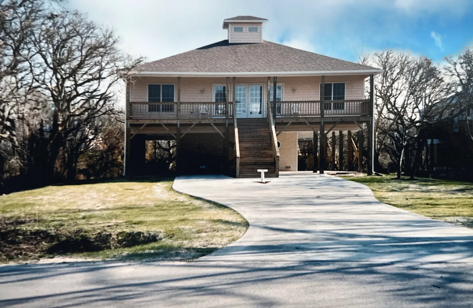 Elevated brick and wood home with hipped roof, deck, and curved concrete driveway