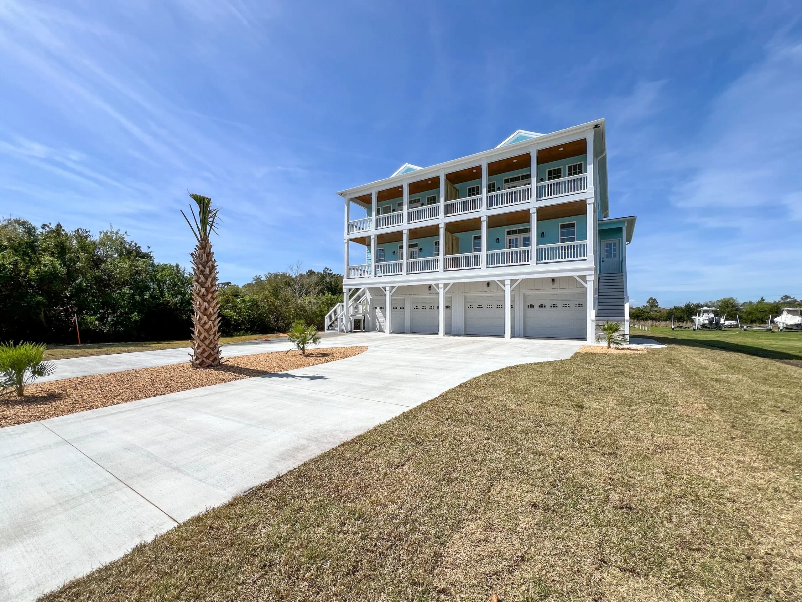 Three-story elevated home with white siding, covered porches, railings, and four-car garage