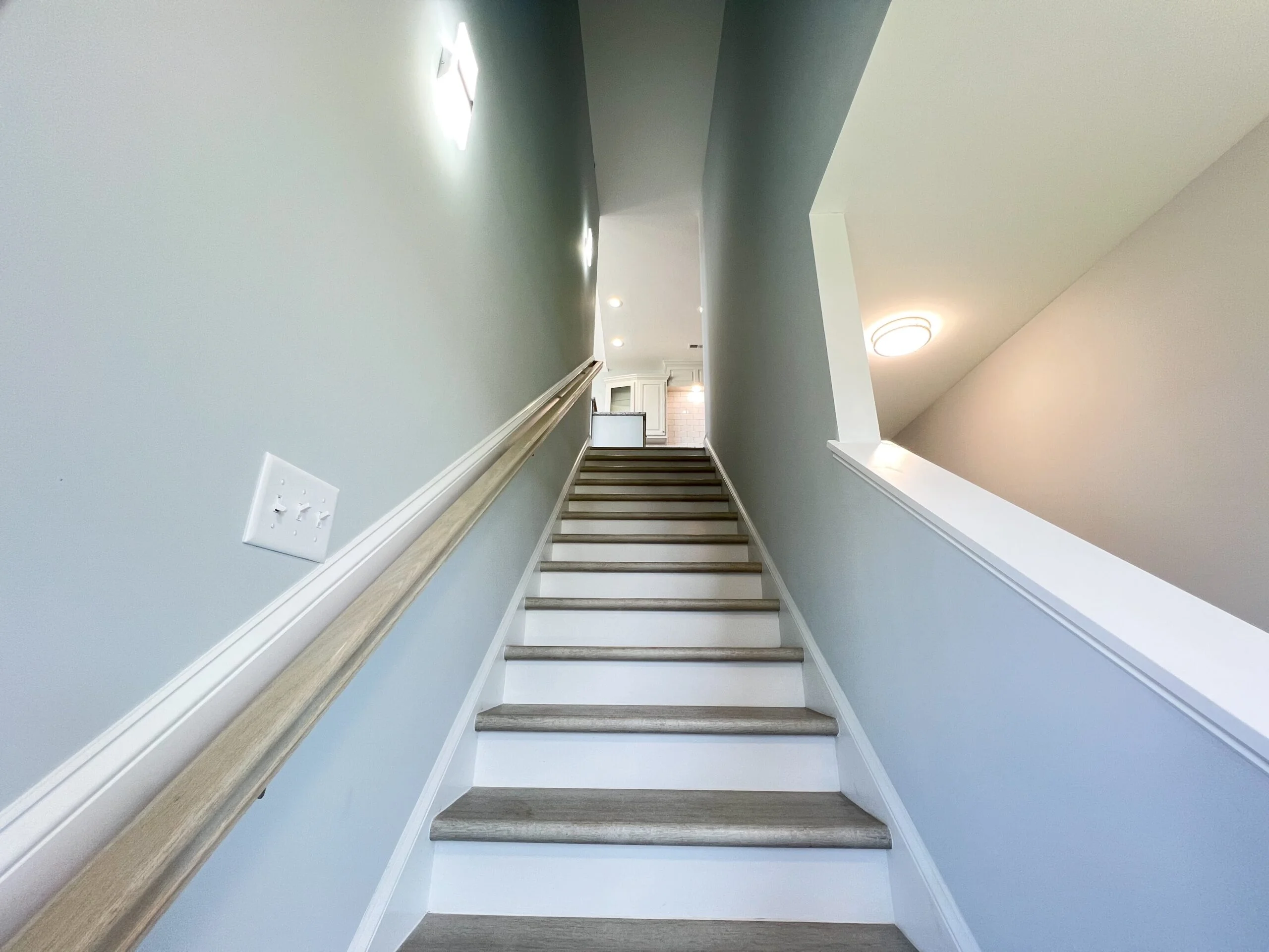 Interior staircase with wood treads, white risers, handrails, and recessed lighting in renovated hallway