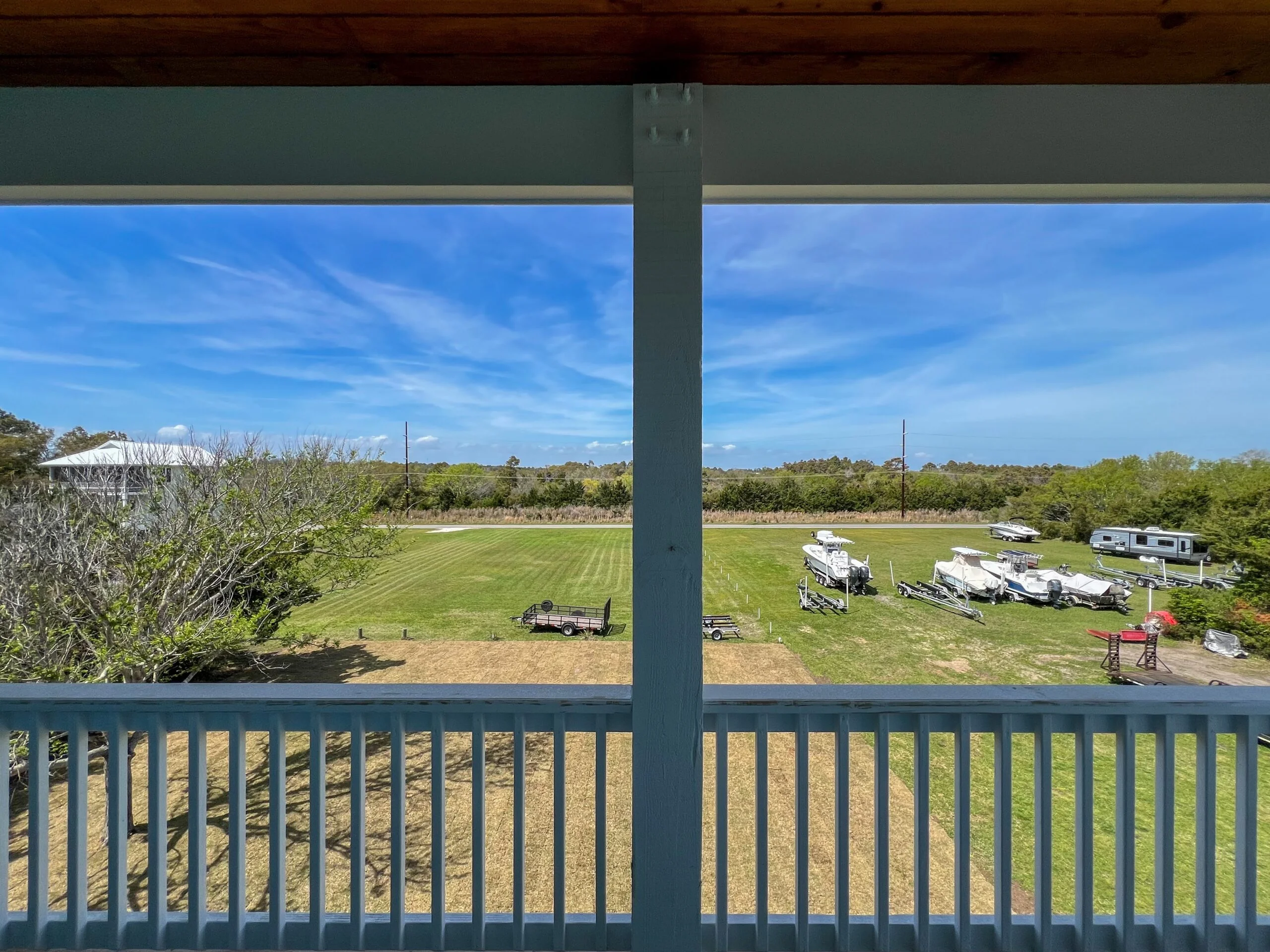 Graded lawn with RV parking spaces, utility poles, and rural property development viewed from covered deck