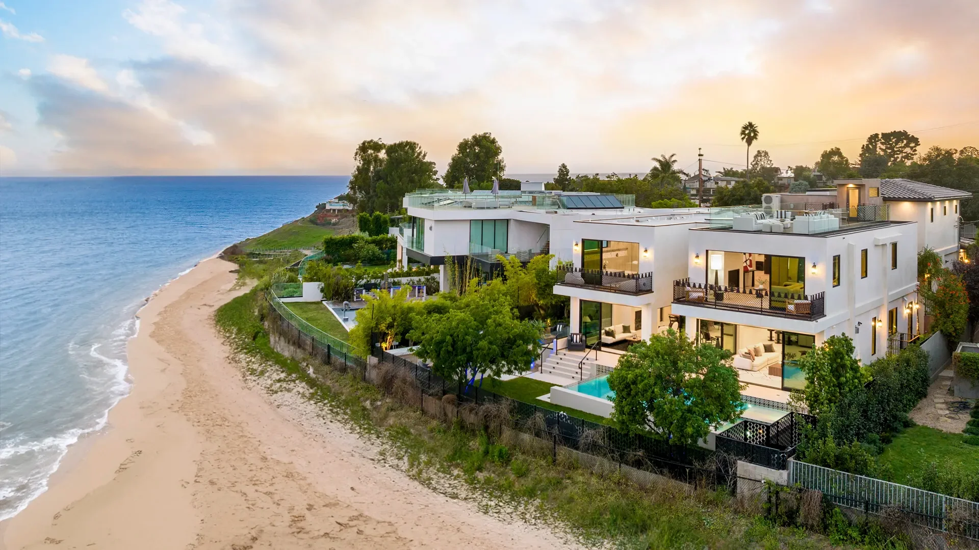 Modern white stucco beachfront home with glass doors, multiple decks, and pool overlooking sandy beach