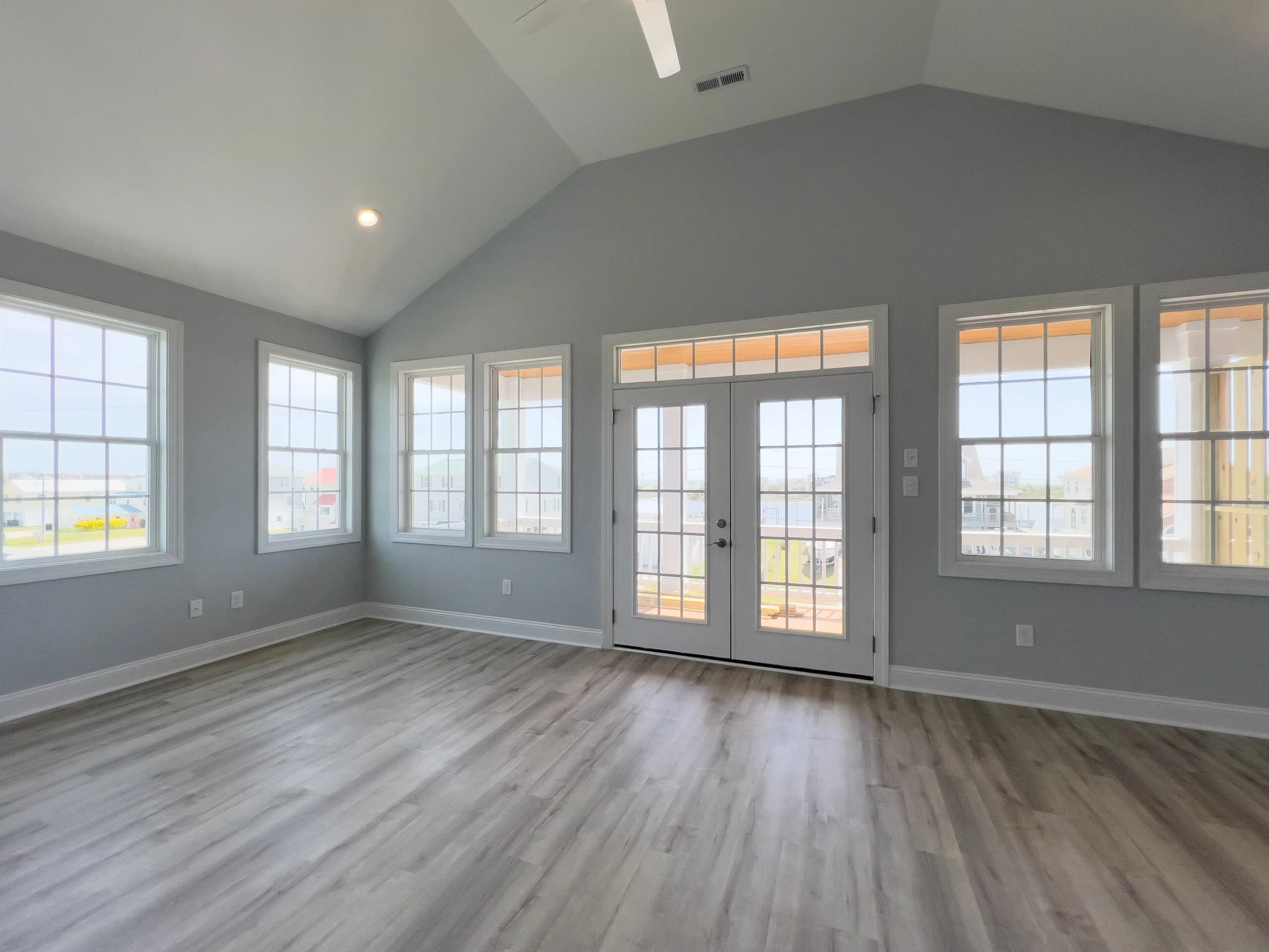 Vaulted sunroom with gray walls, vinyl plank flooring, French doors, and multiple casement windows
