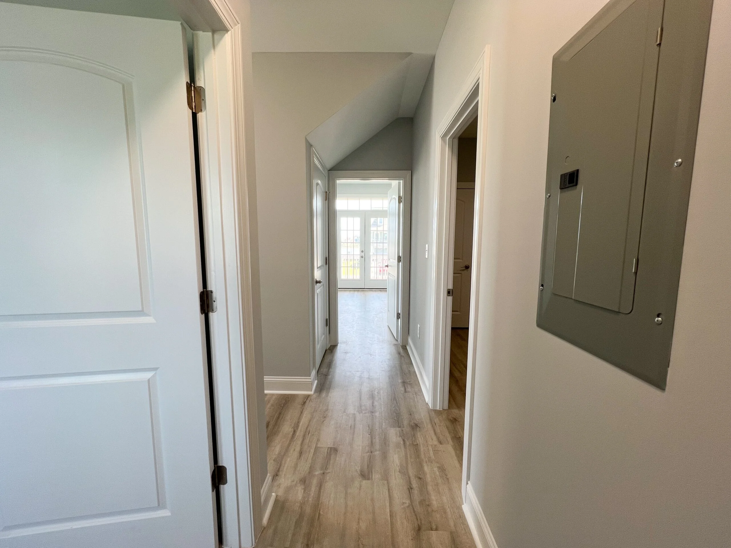 Hallway with vinyl plank flooring, white trim, painted walls, and electrical panel