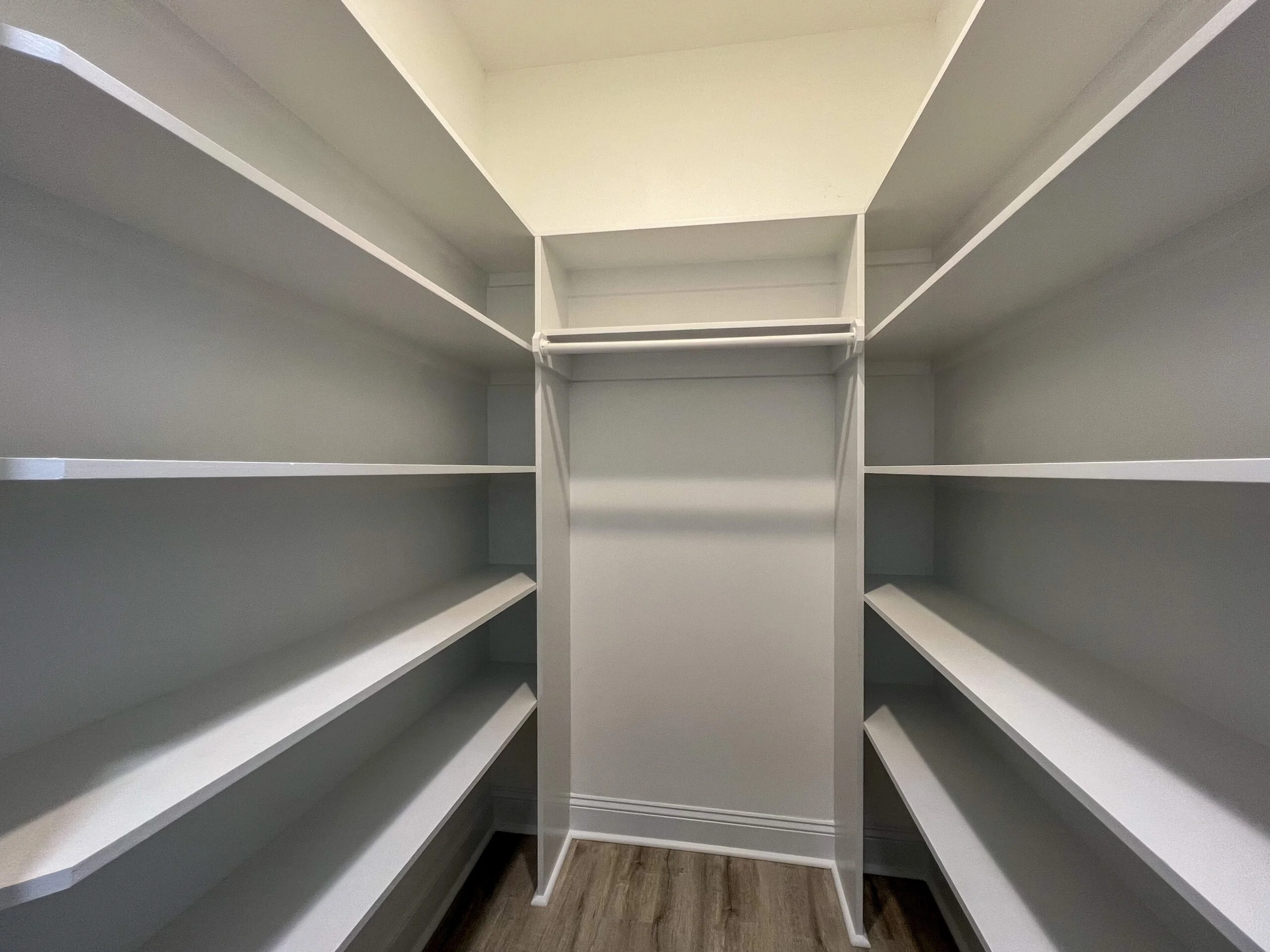 Walk-in closet with white-trimmed shelving, gray walls, and wood flooring